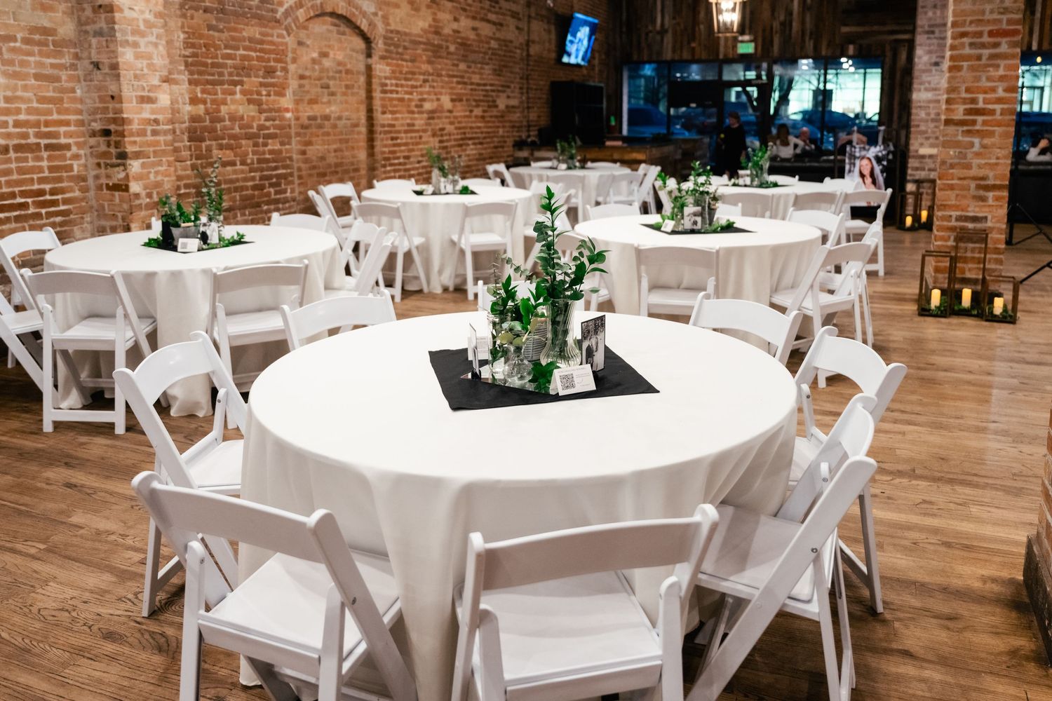 Table set up for a wedding reception in a rustic brick venue with greenery centerpieces. Utah Wedding Photographer at Southworth Hall.