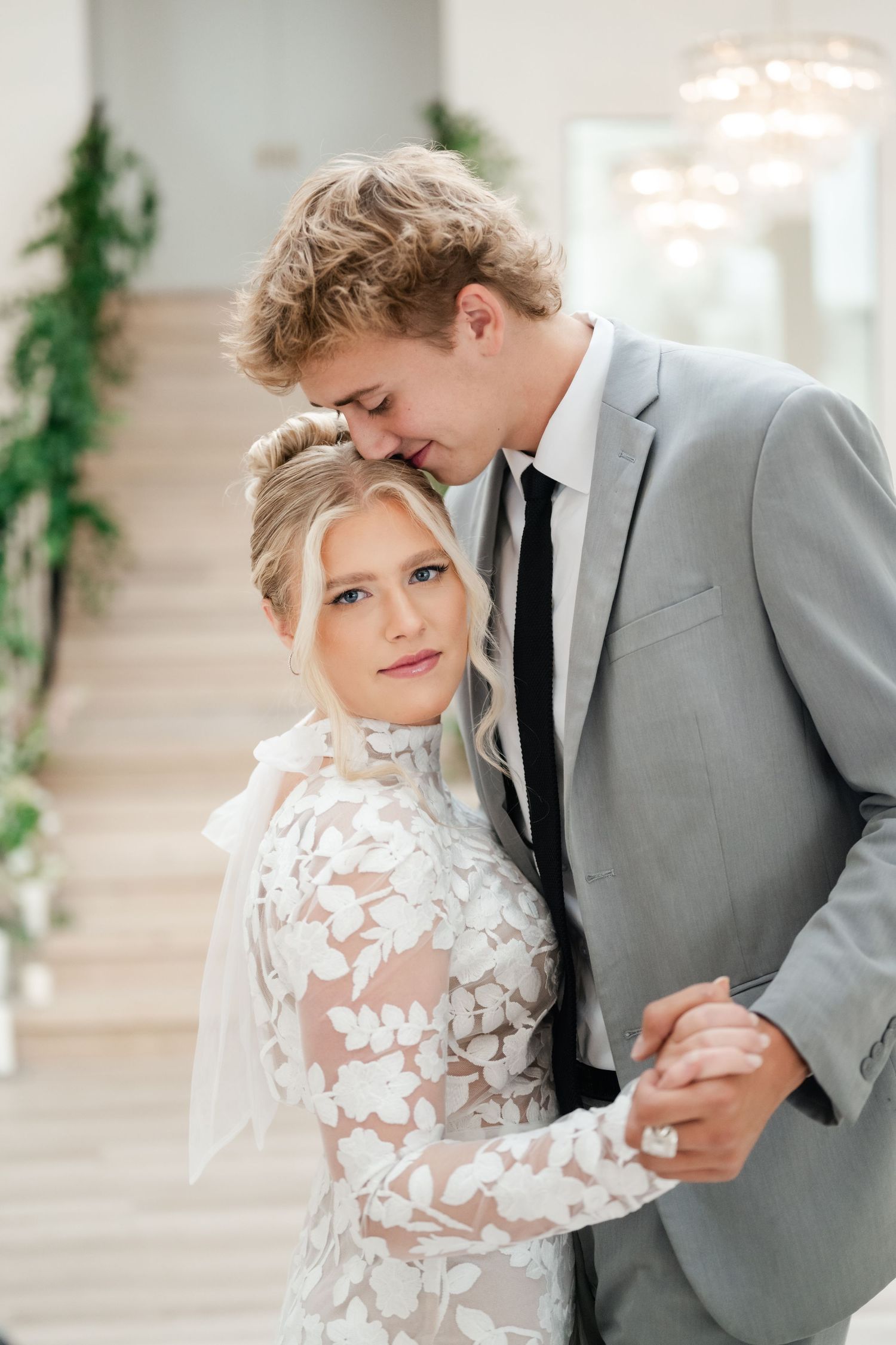 A couple in wedding attire hug, with the bride wearing a delicate lace gown and groom in a gray suit. Utah County wedding venues.