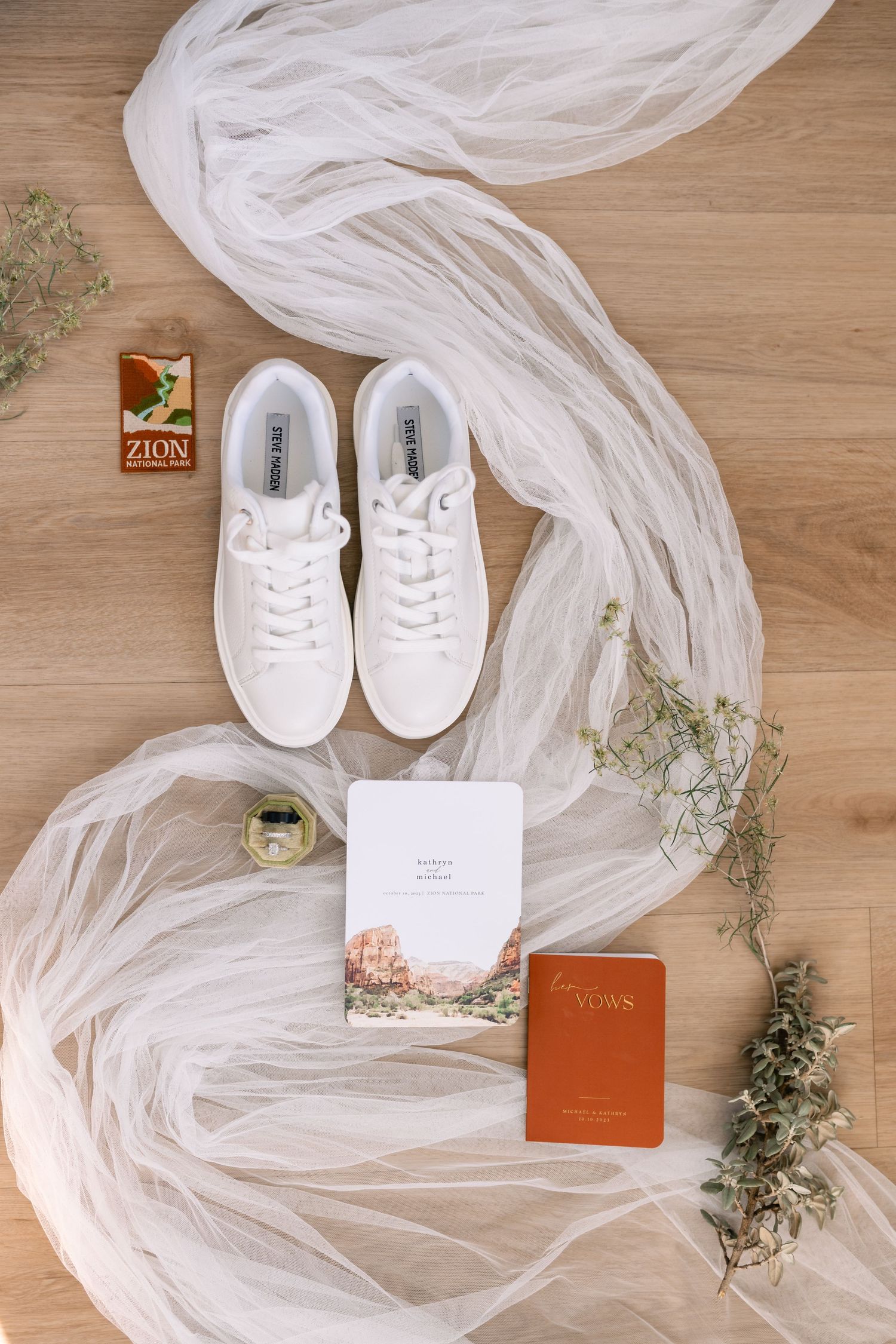 Bridal flatlay with white veil, sneakers, and wedding accessories on wooden surface.