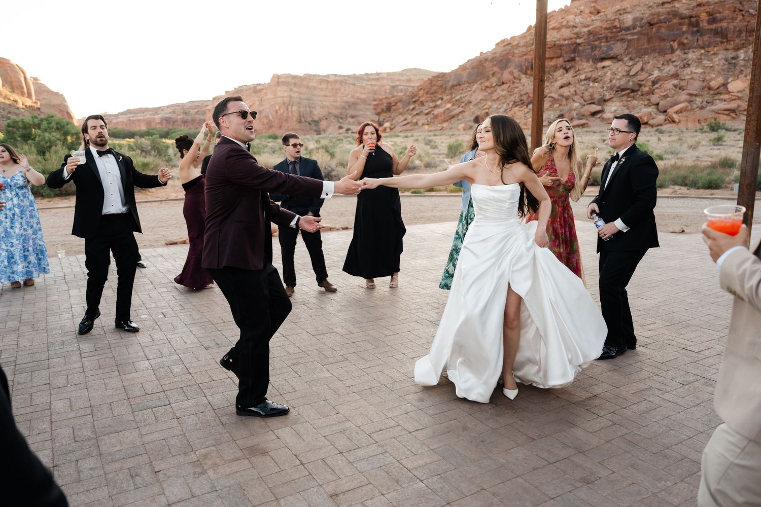 Bride and groom dancing outdoors at desert wedding reception with red rock canyon backdrop and guests watching.