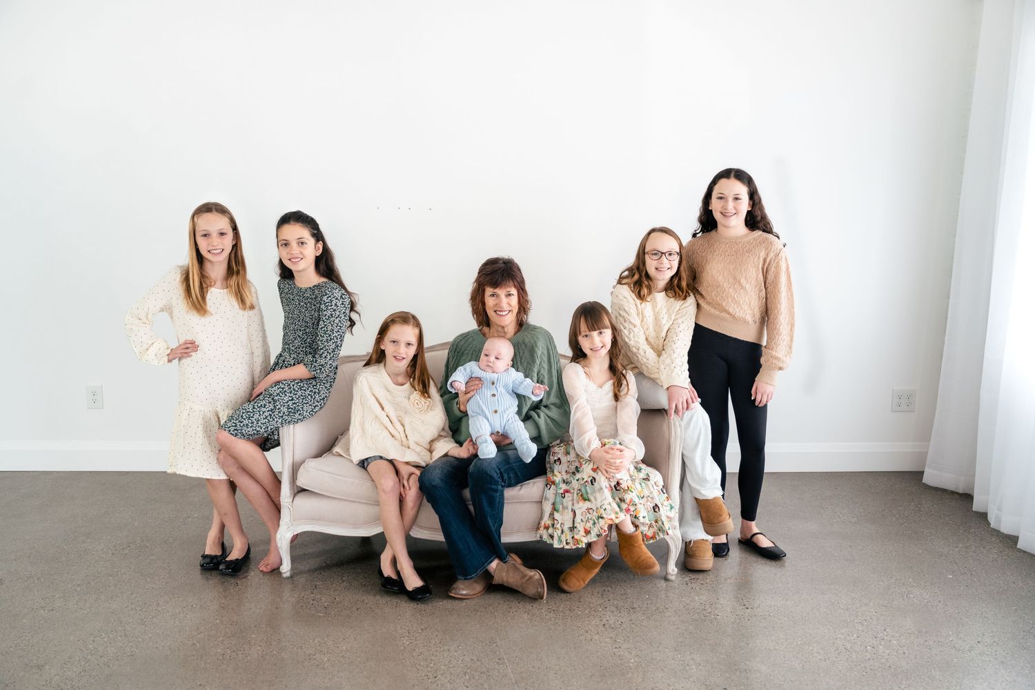 Group of people sitting casually against a white wall in a minimalist studio setting.