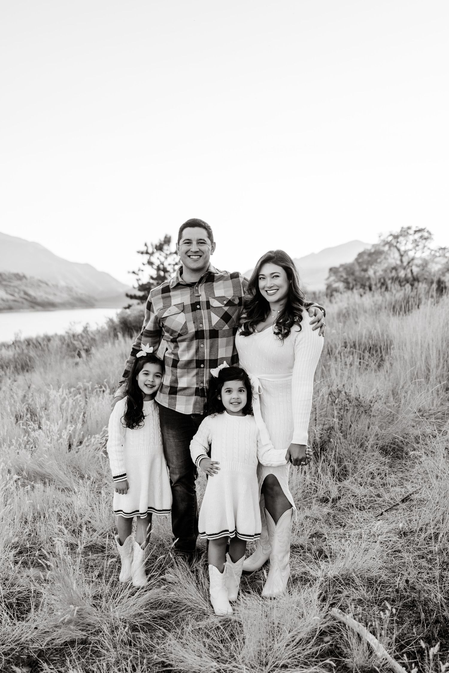 A family poses together on a grassy hillside overlooking a lake and mountains in black and white.