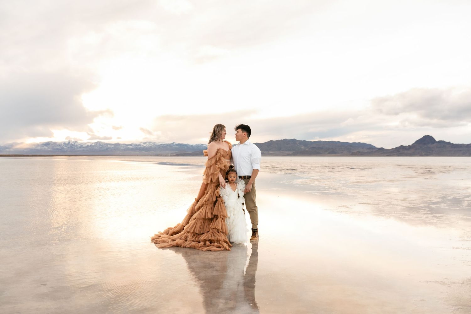 Couple in elegant attire poses romantically on white sandy beach during sunset photo session. Utah Salt Flats Photographer.