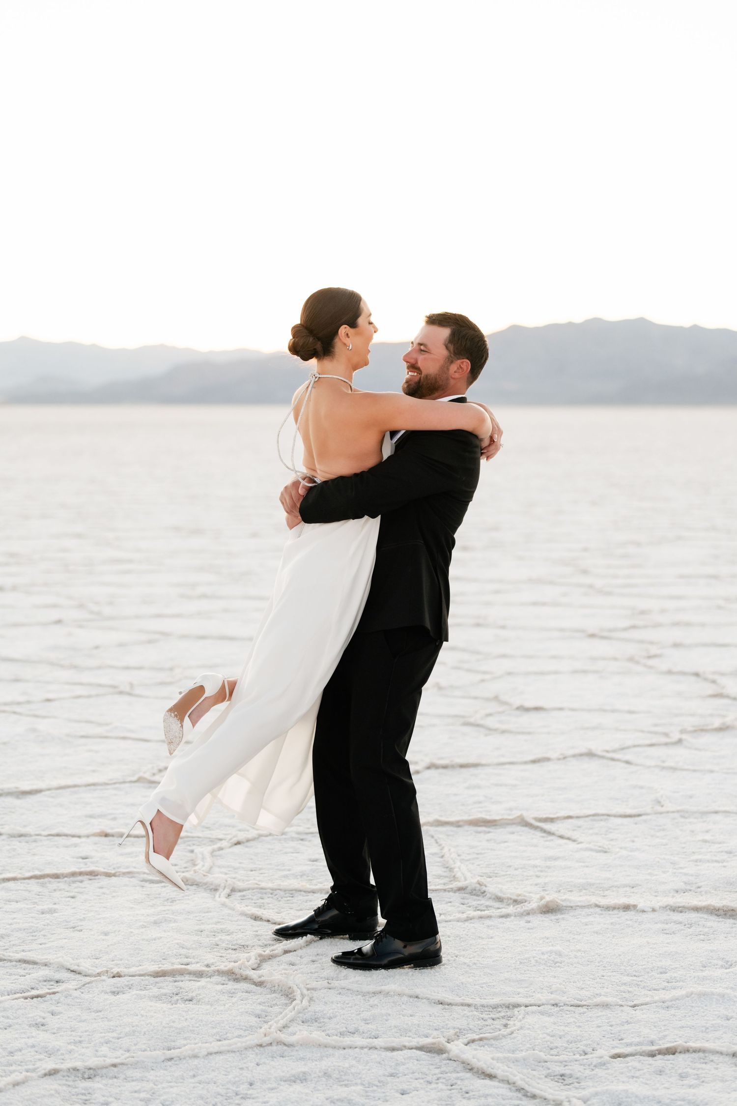 Utah Salt Flats Photographer. Joyful lift pose in formal wear on the salt flats at sunset.