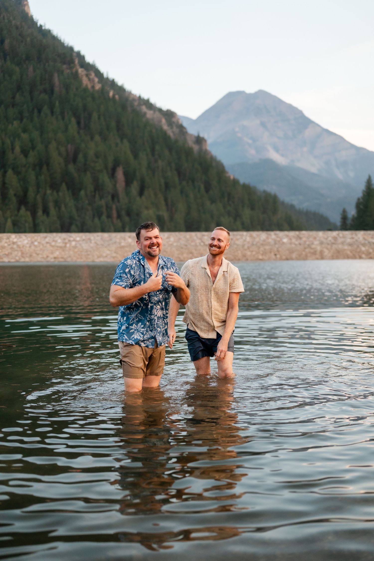 Couple having a water fight at Tibble Fork Reservoir. Two men smiling and standing in a mountain lake wearing casual shirts and shorts.