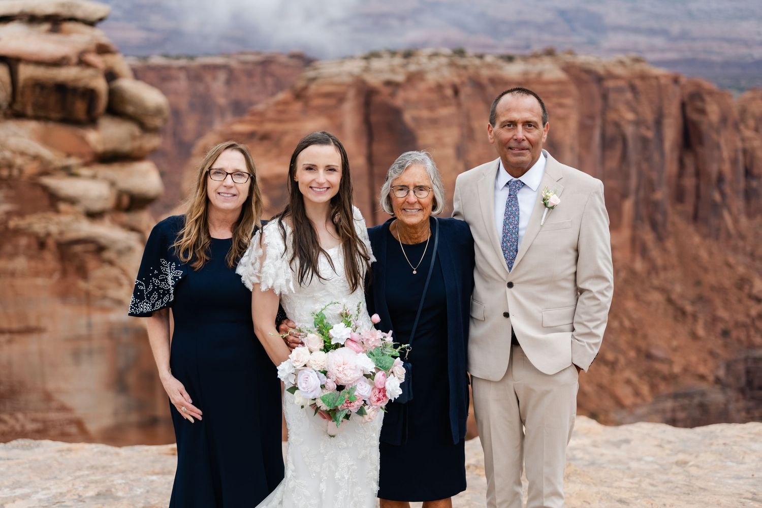 Wedding party poses together on rocky cliff edge with vast canyon landscape behind them.