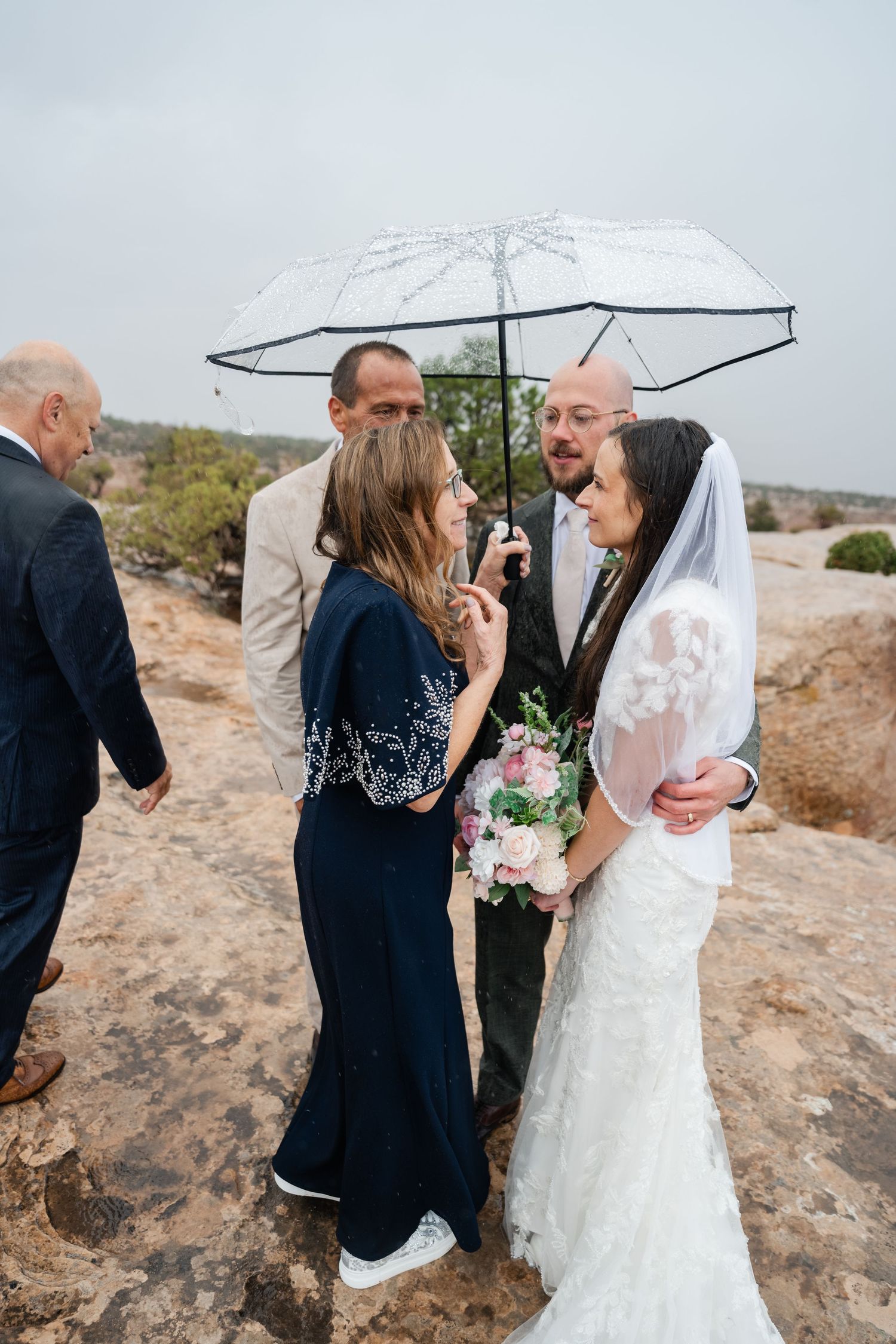 Outdoor desert wedding ceremony under white umbrellas with small gathering of guests.