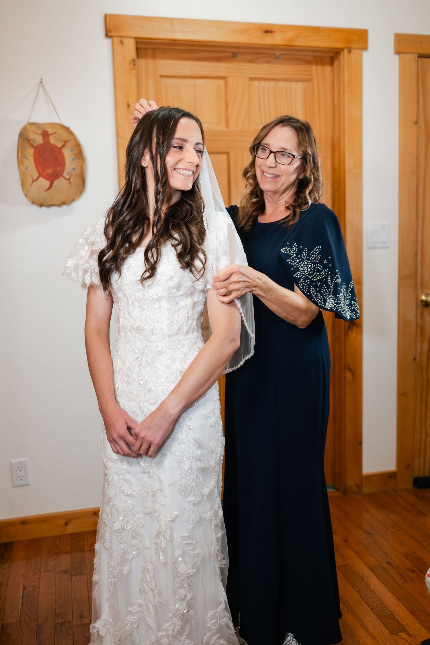 A bride in an elegant lace gown shares a joyful moment during wedding preparations.