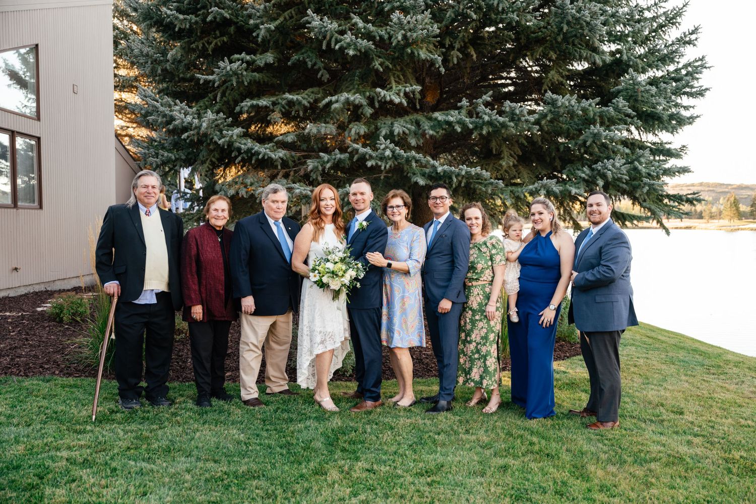Wedding party members gathered for a group photo in front of a large evergreen tree.