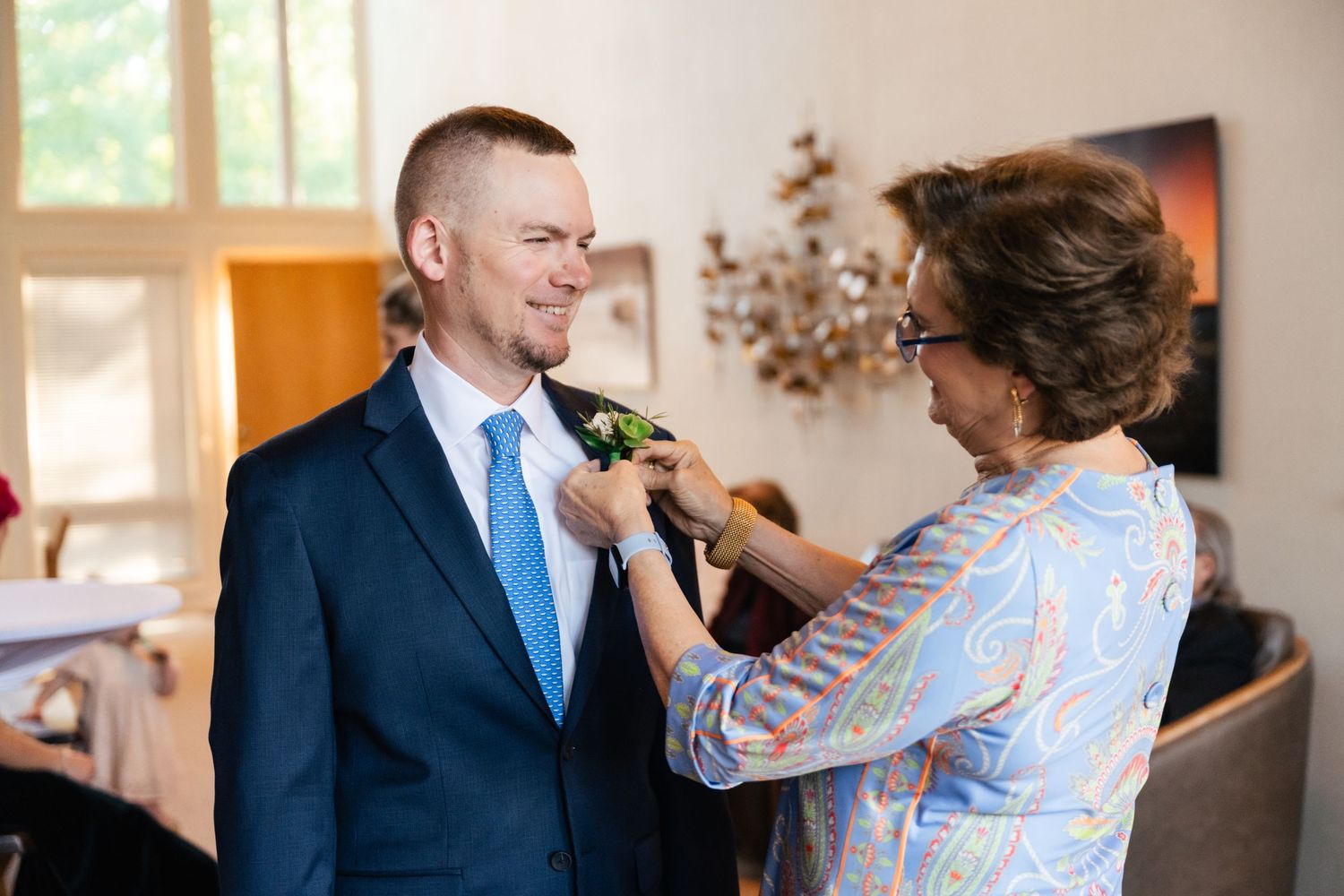 A boutonniere is being pinned onto a navy suit jacket during wedding preparations.