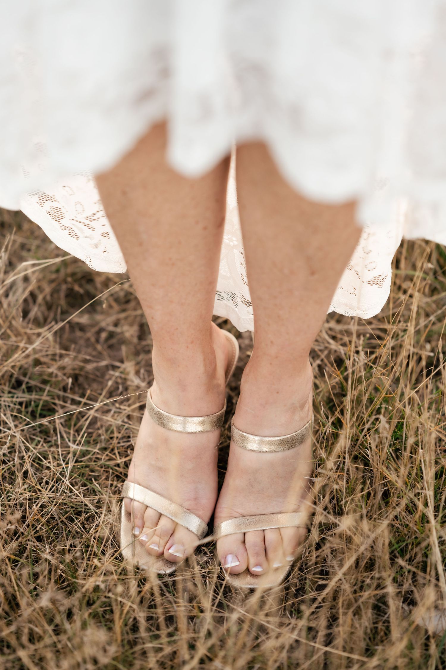 Gold strappy sandals on bride's feet in tall grass.