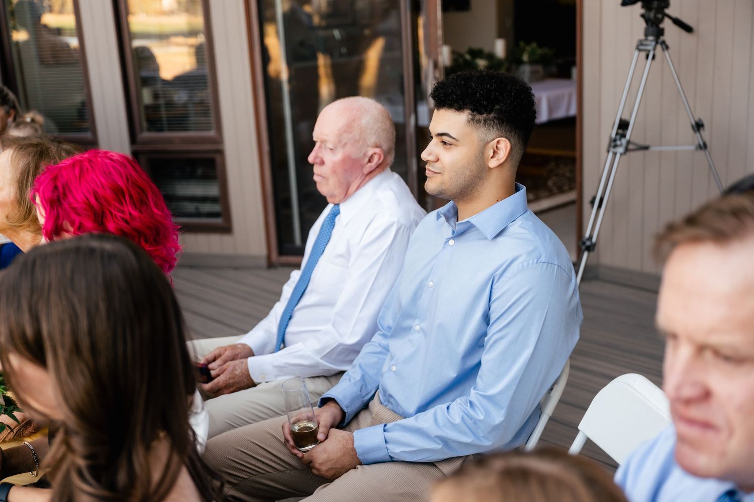 Wedding guests seated on folding chairs during an outdoor ceremony.