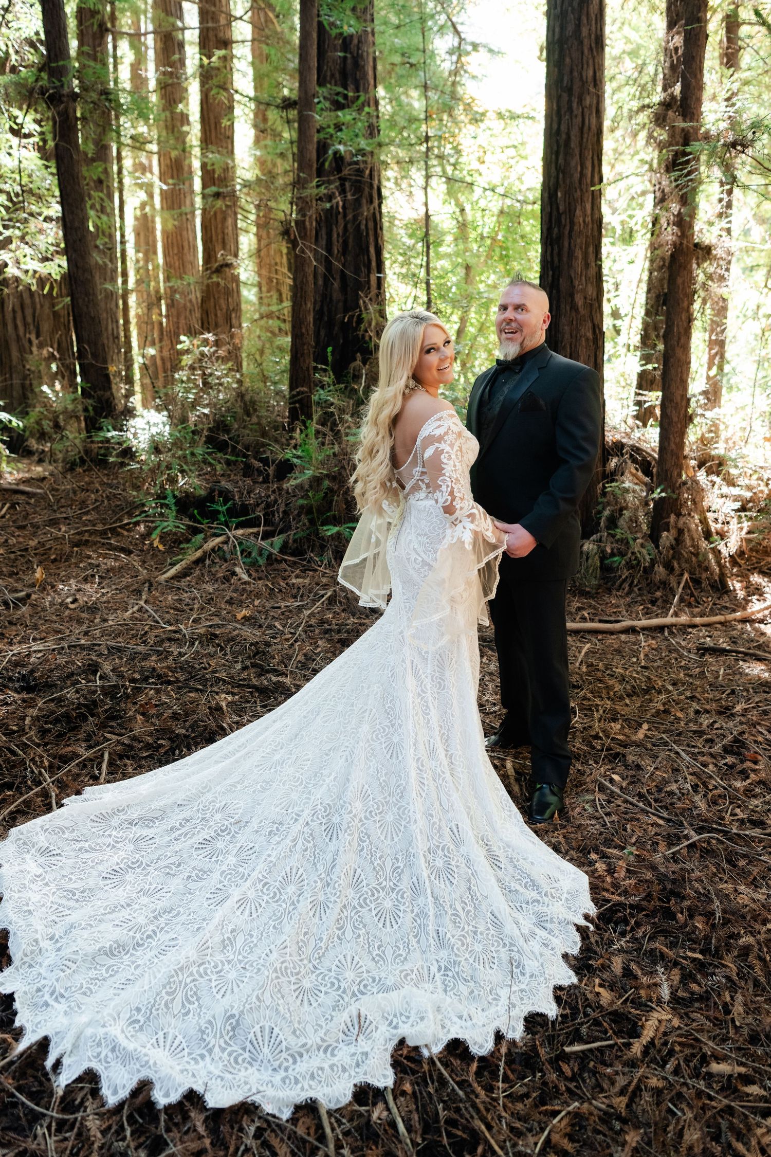 Stunning lace wedding dress with dramatic cathedral train displayed in a forest setting.
