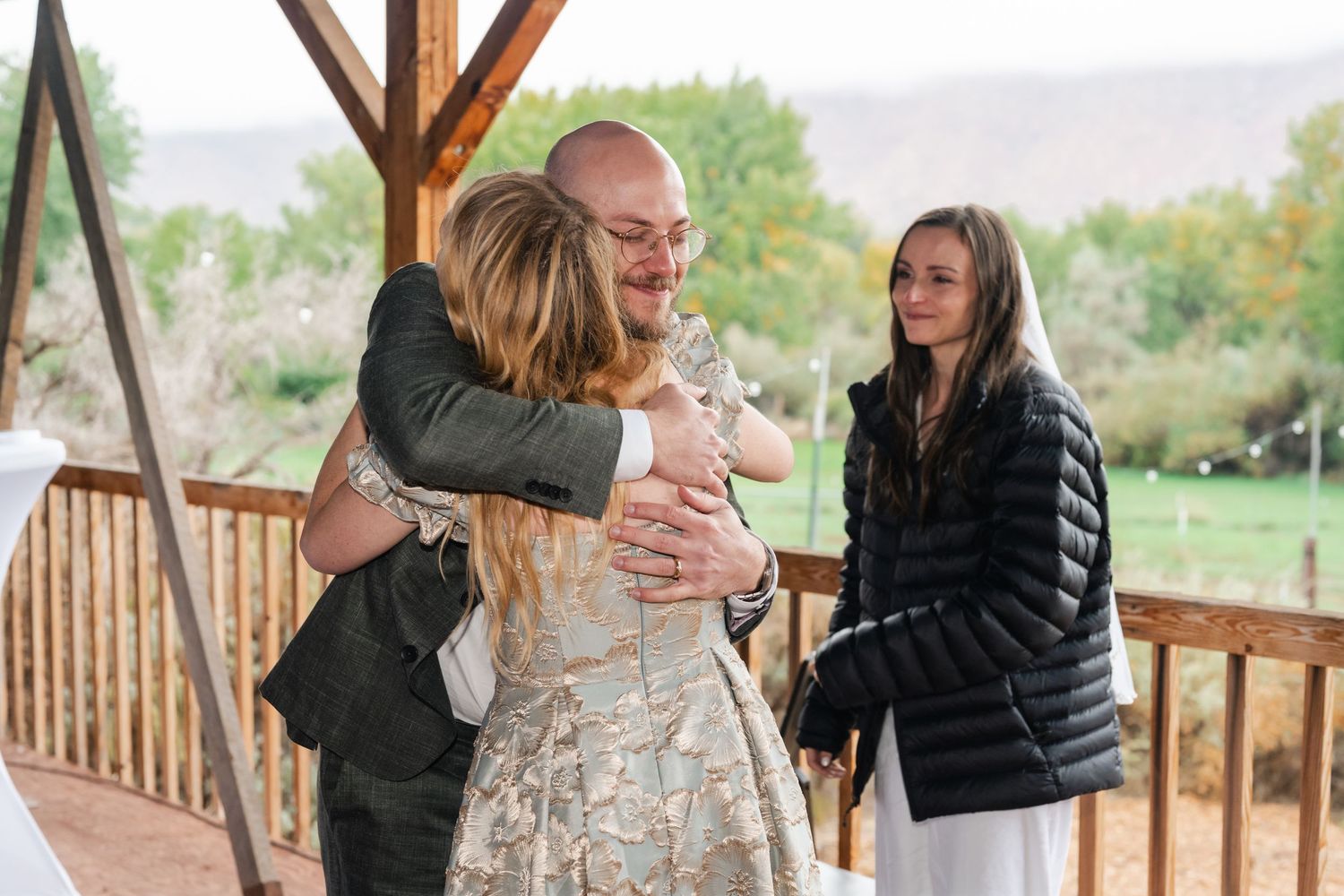 Guests celebrate at an outdoor wedding venue with wooden railings and fall foliage.