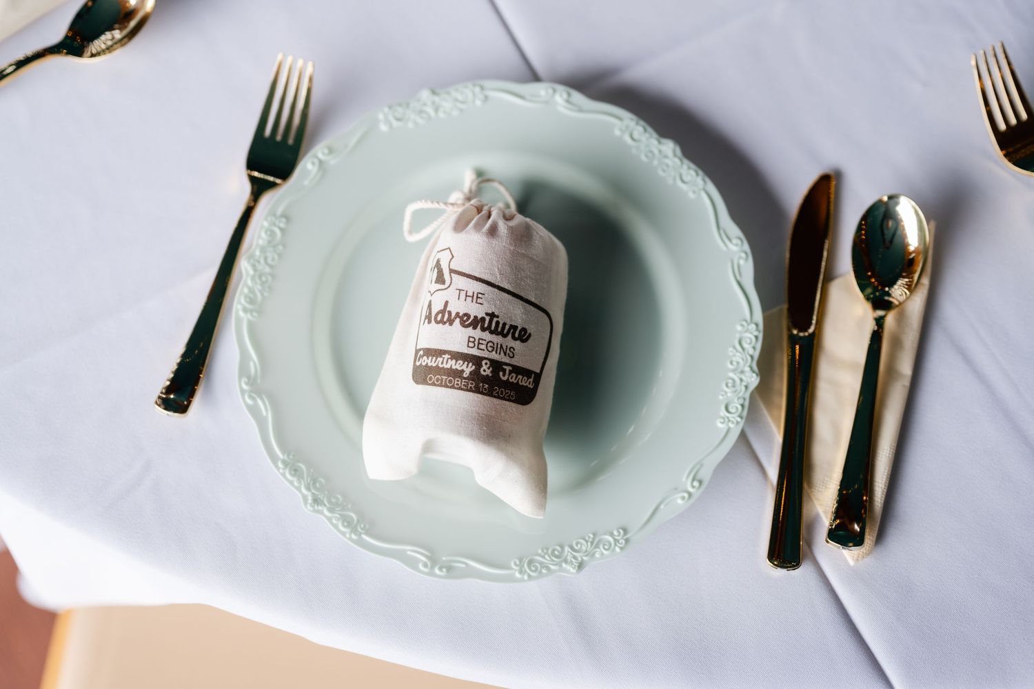 Elegant place setting with mint green plates and gold cutlery on a light gray tablecloth.