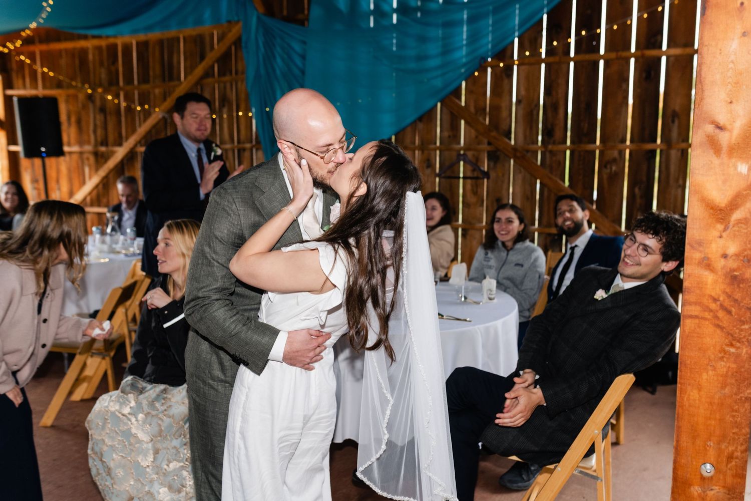 People dancing and celebrating under blue fabric draped from wooden beams at an evening event.