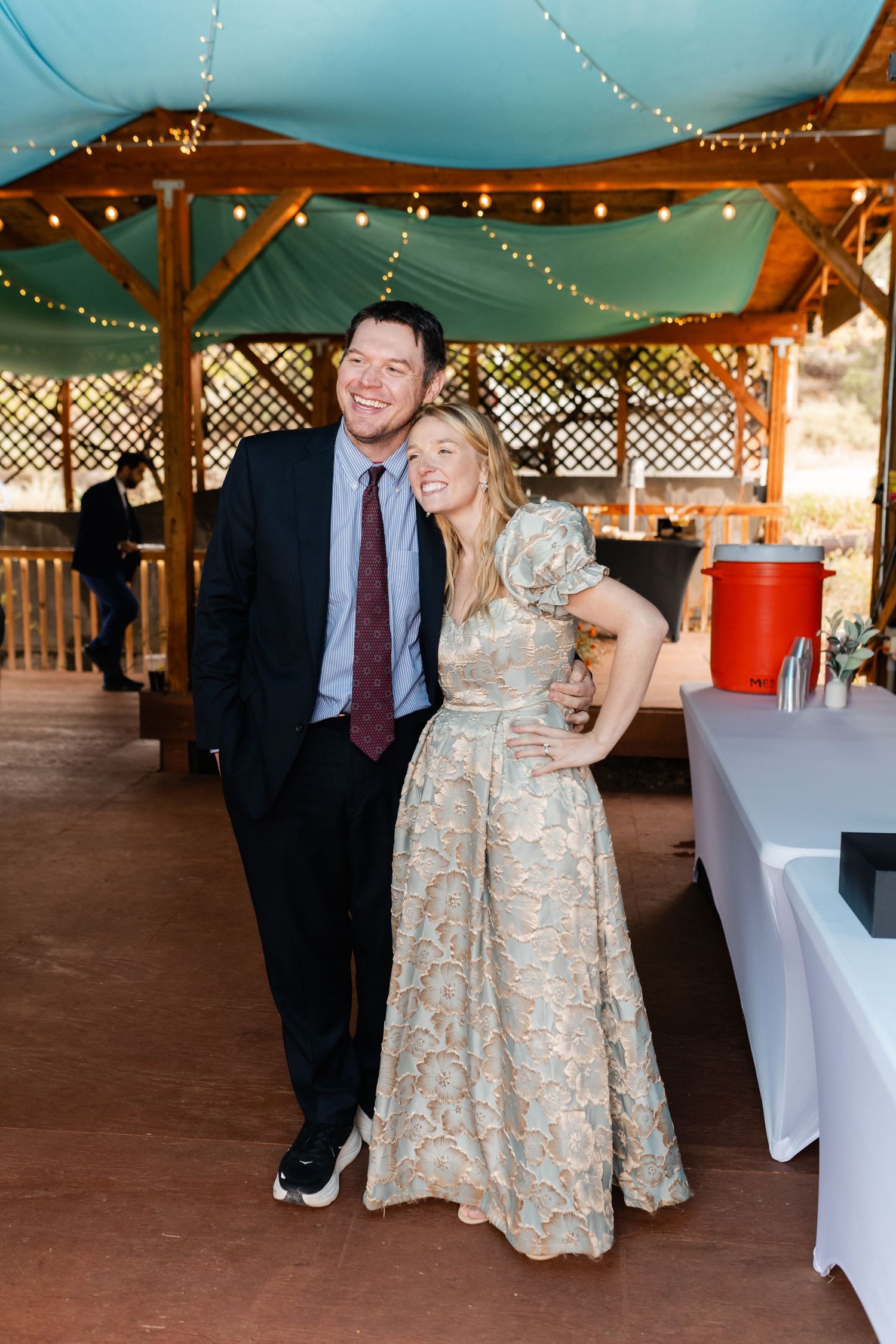 A couple dances together at a wedding reception under twinkling lights and teal decor.