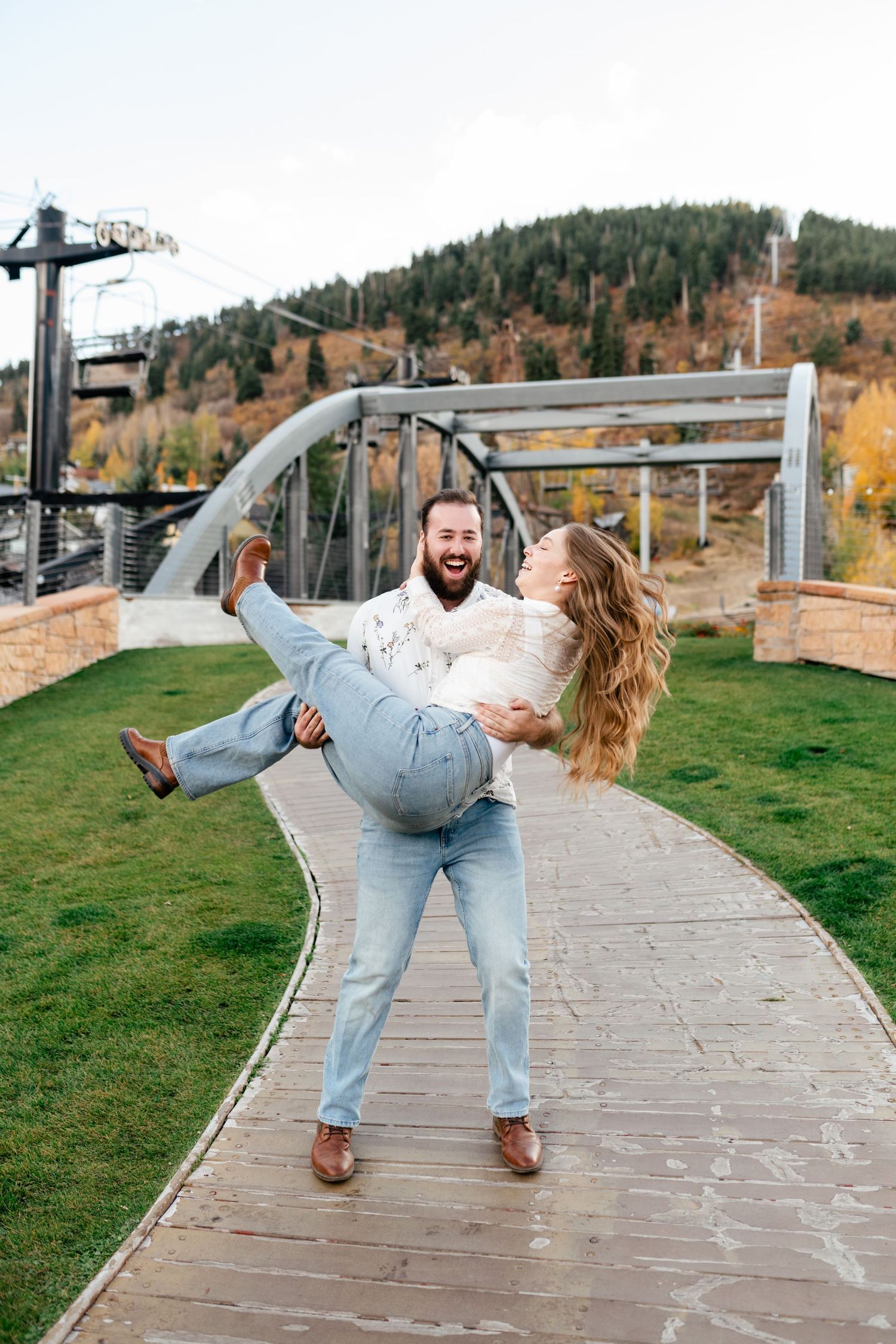 Joyful couple shares a playful moment with autumn mountains and ski lift in the background. Best Park City Engagement Photographer.
