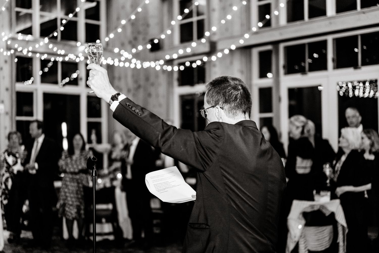 A person at a wedding reception raises their arm while dancing beneath twinkling string lights and windows. Park City Wedding Photographer.