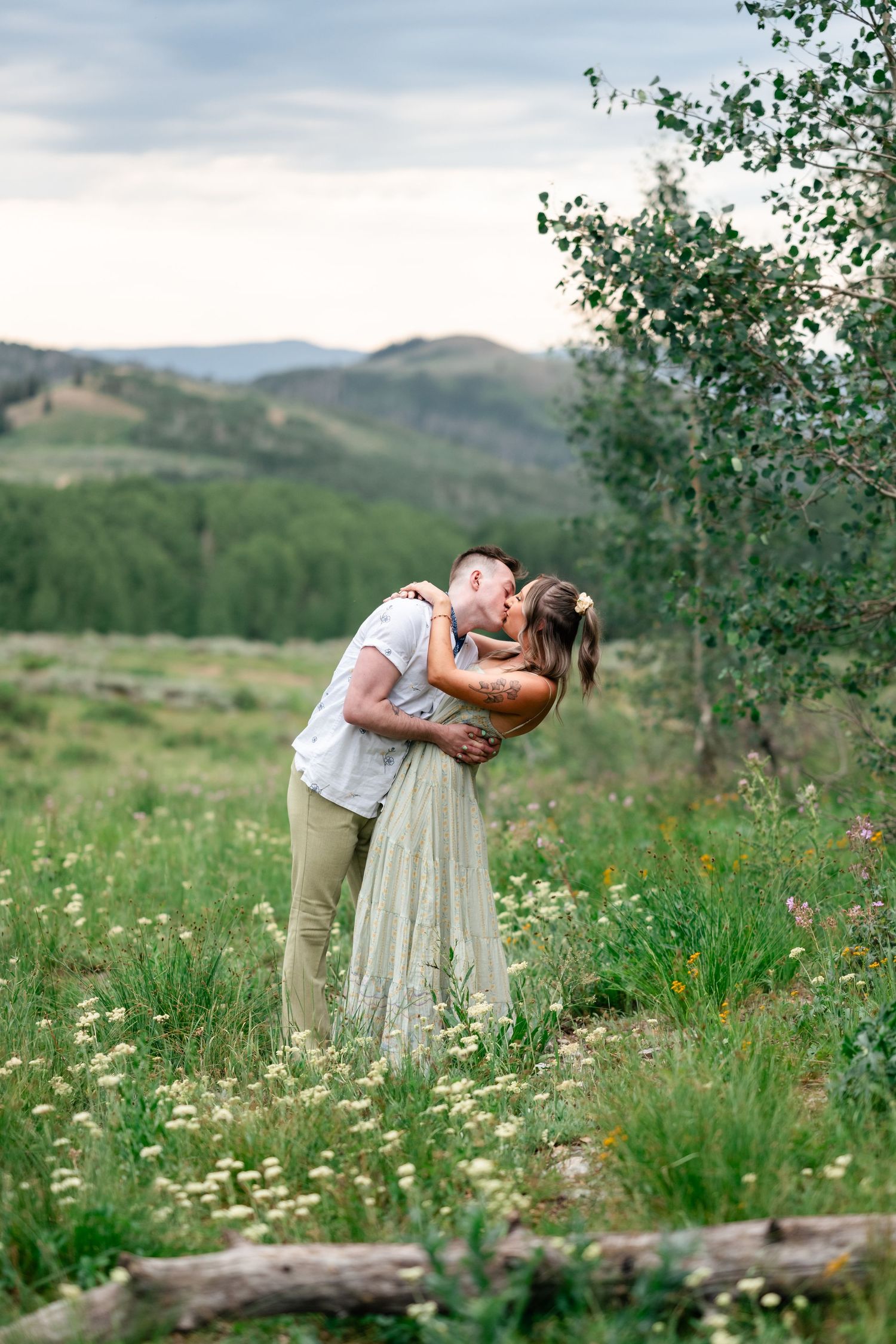 A romantic couple embraces in a mountain meadow filled with wildflowers during a summer photoshoot. Park City engagement photographer.