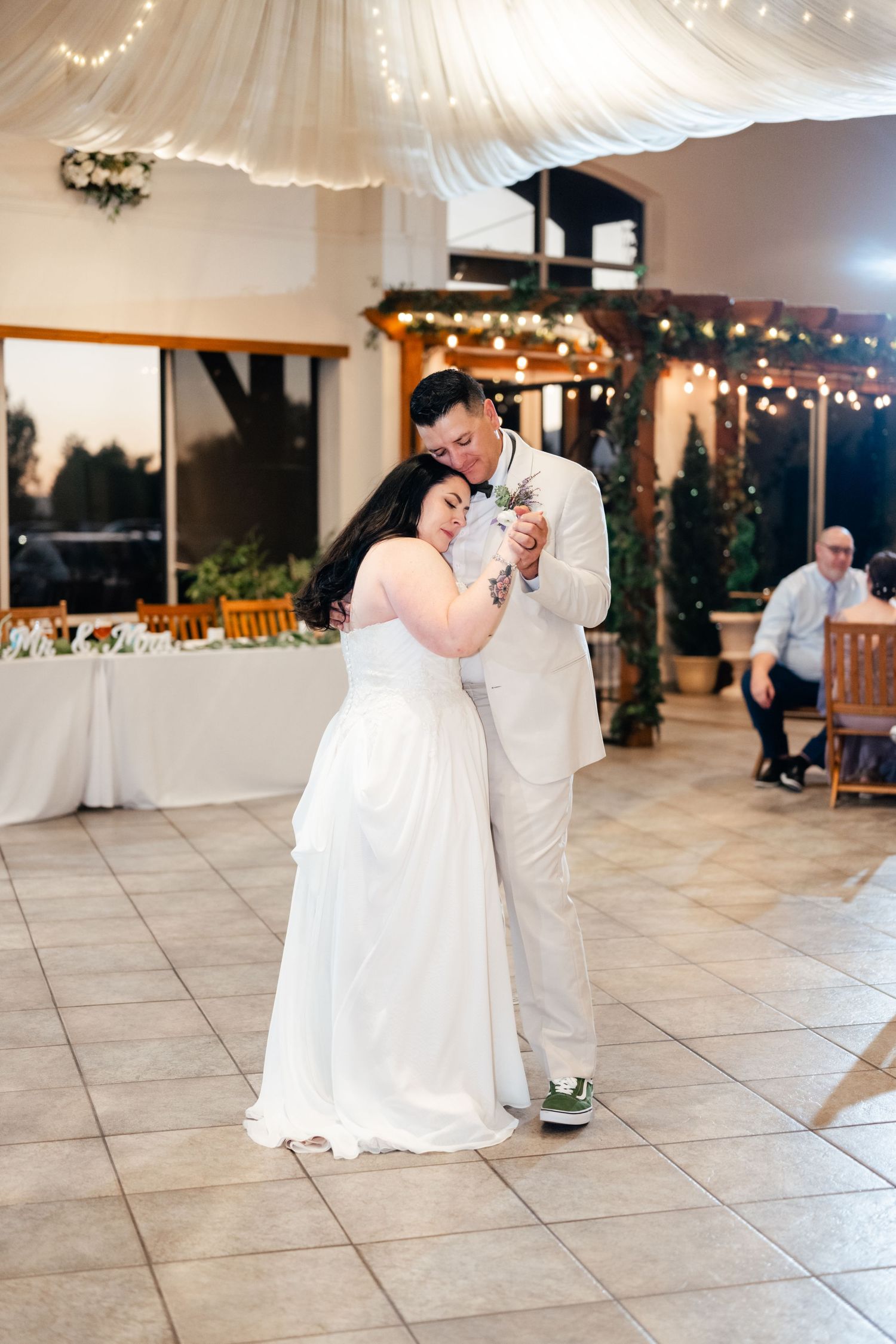 A couple shares their first dance at a wedding reception under string lights and white drapes in an elegant venue.