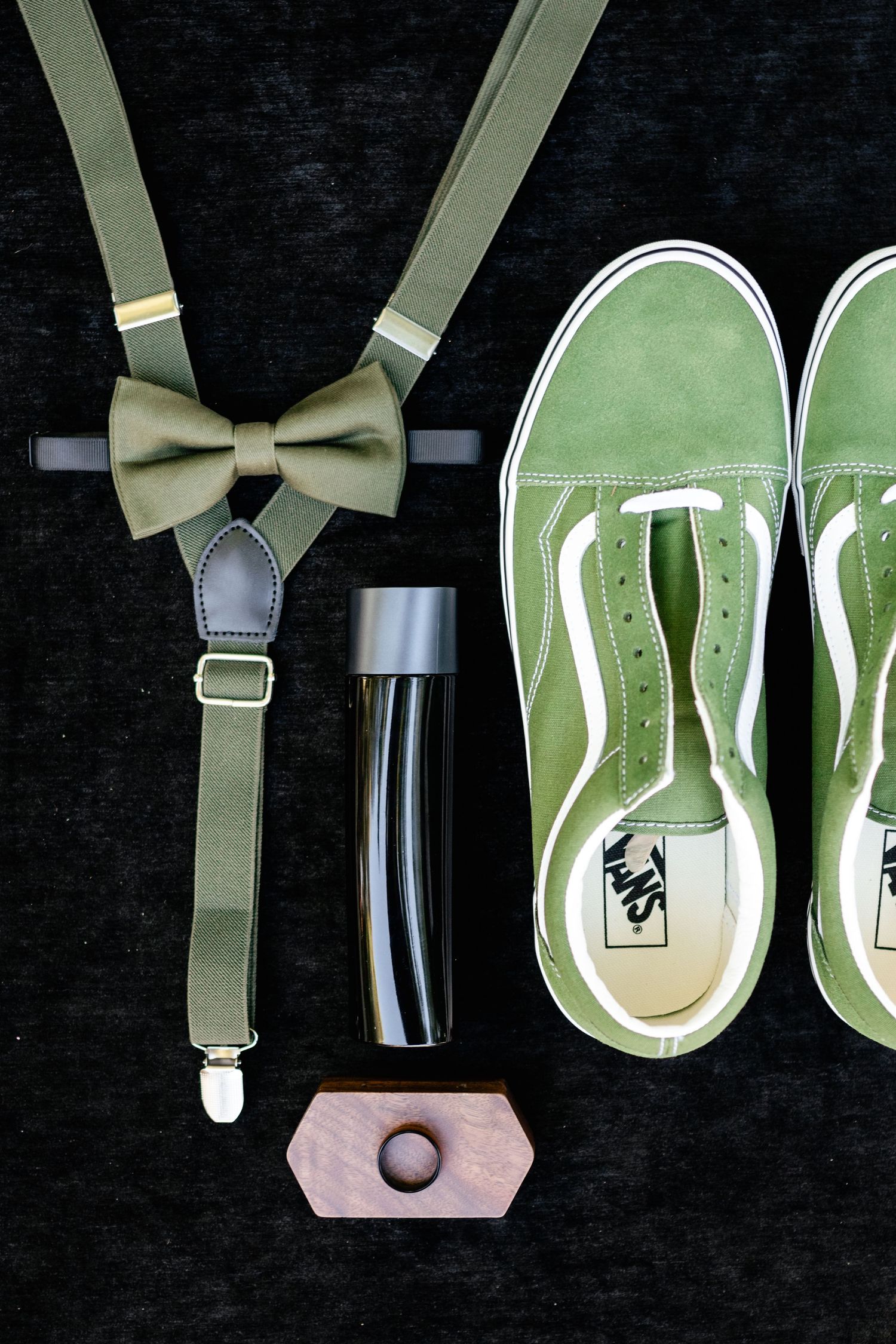 Sage green accessories including suspenders with bow tie, Vans sneakers and a water bottle arranged on black background.