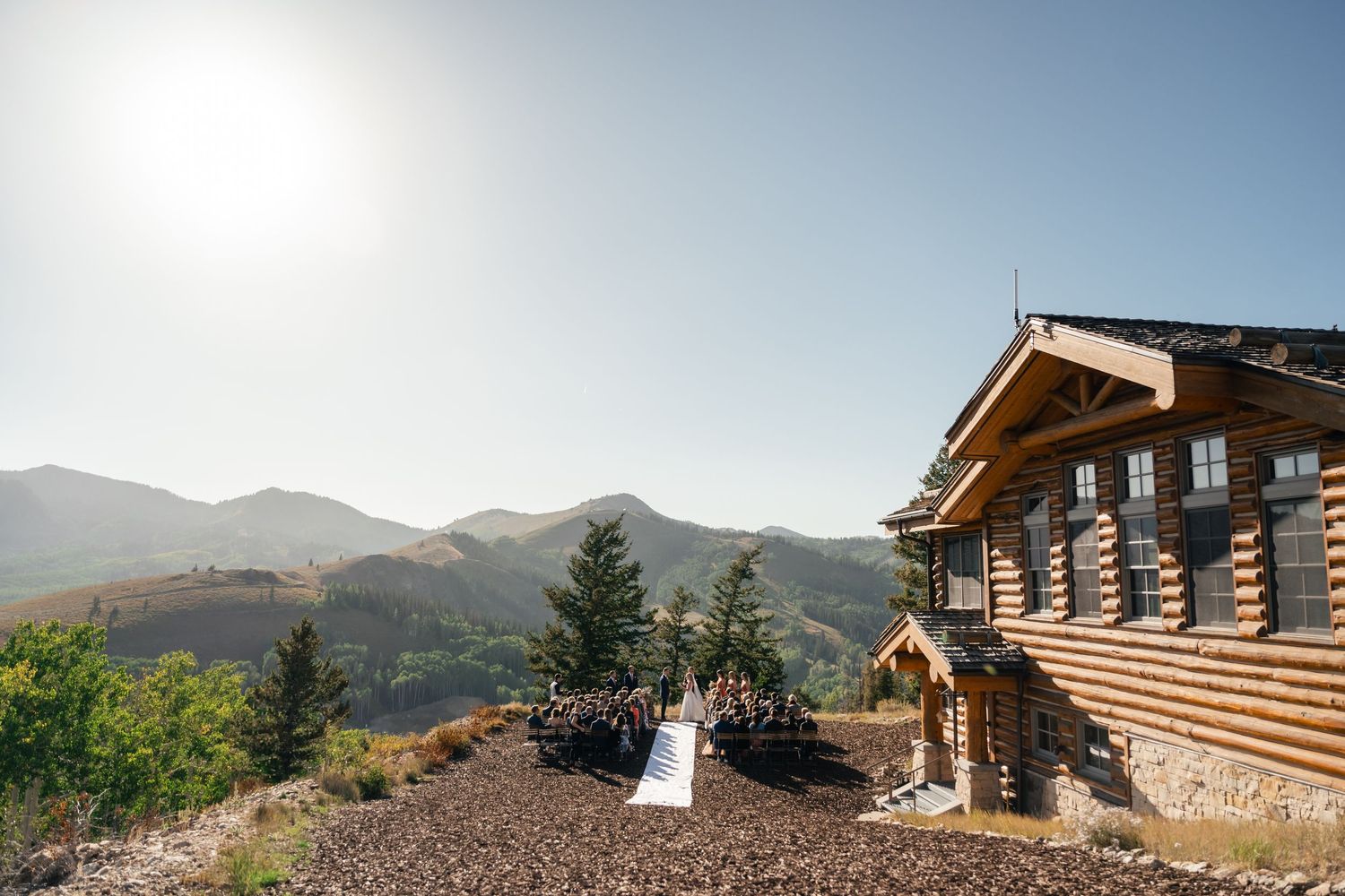 A mountain cabin perched on a scenic hillside with sweeping mountain views under a bright, clear sky.
