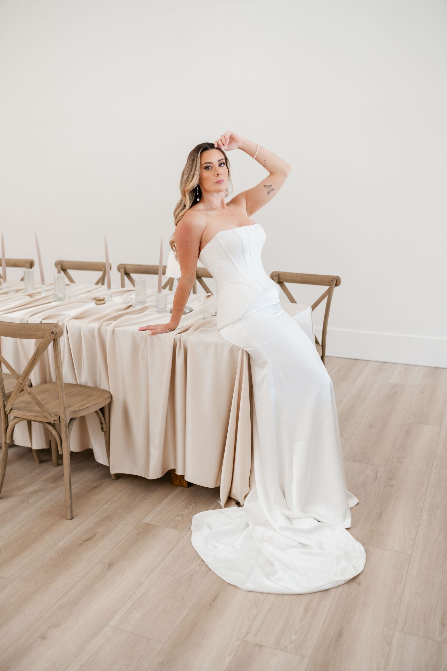 Elegant strapless wedding dress with long train displayed against rustic wooden chairs in minimalist setting. Moments on Main Photographer.