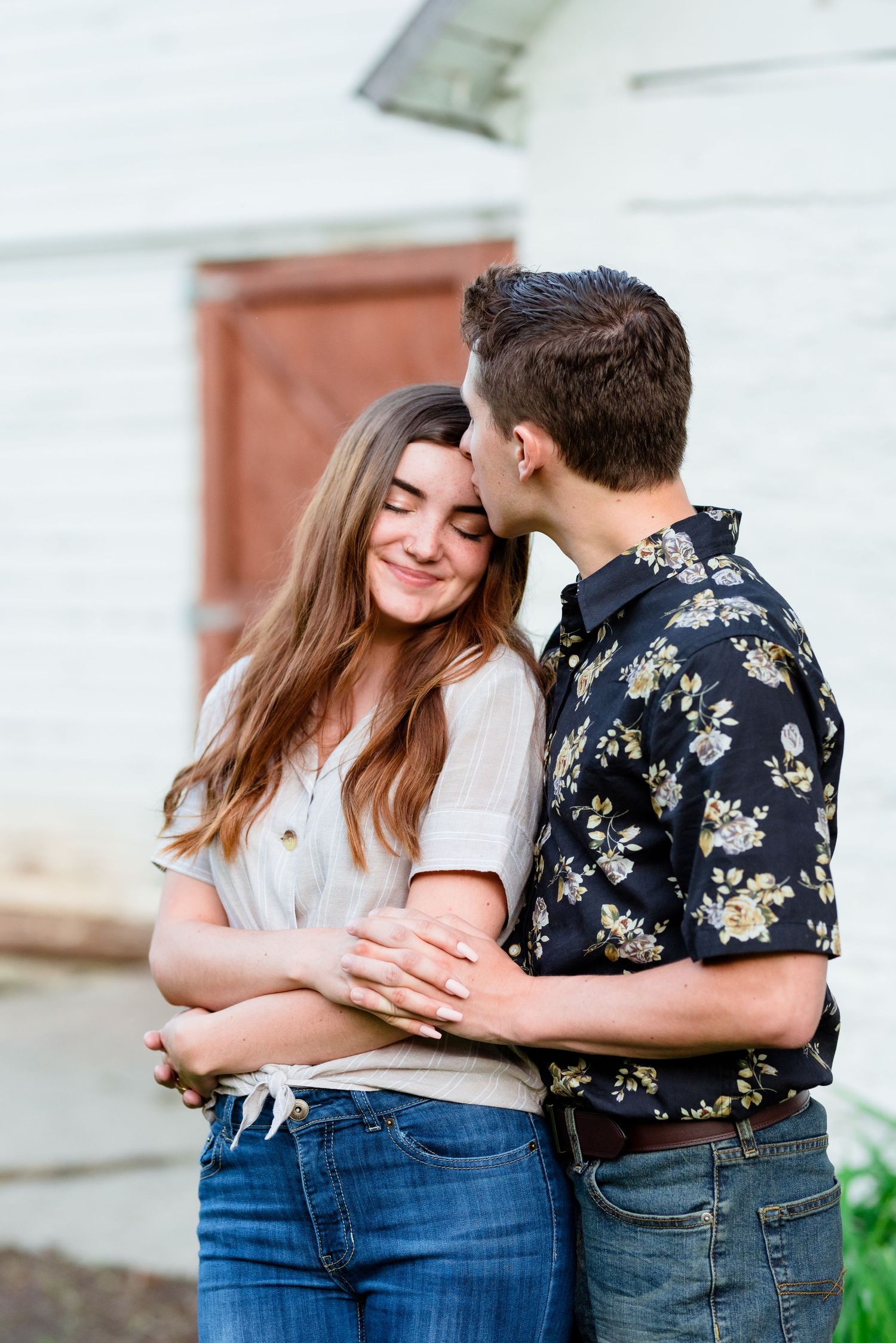 A couple shares an intimate moment while embracing outside a white building.