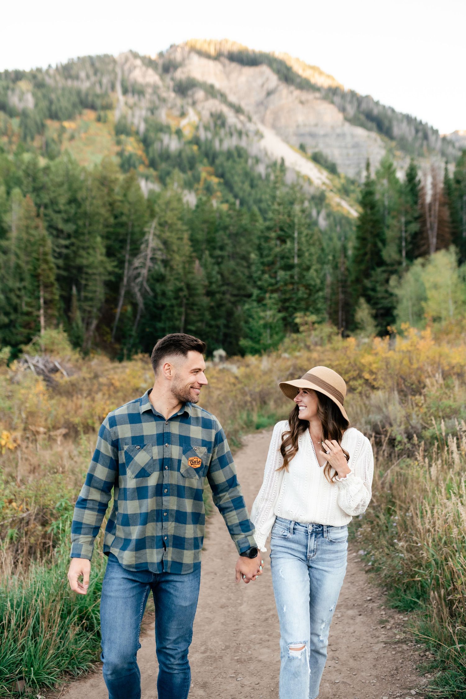 A couple walking hand in hand on a mountain trail with rugged peaks in the background.