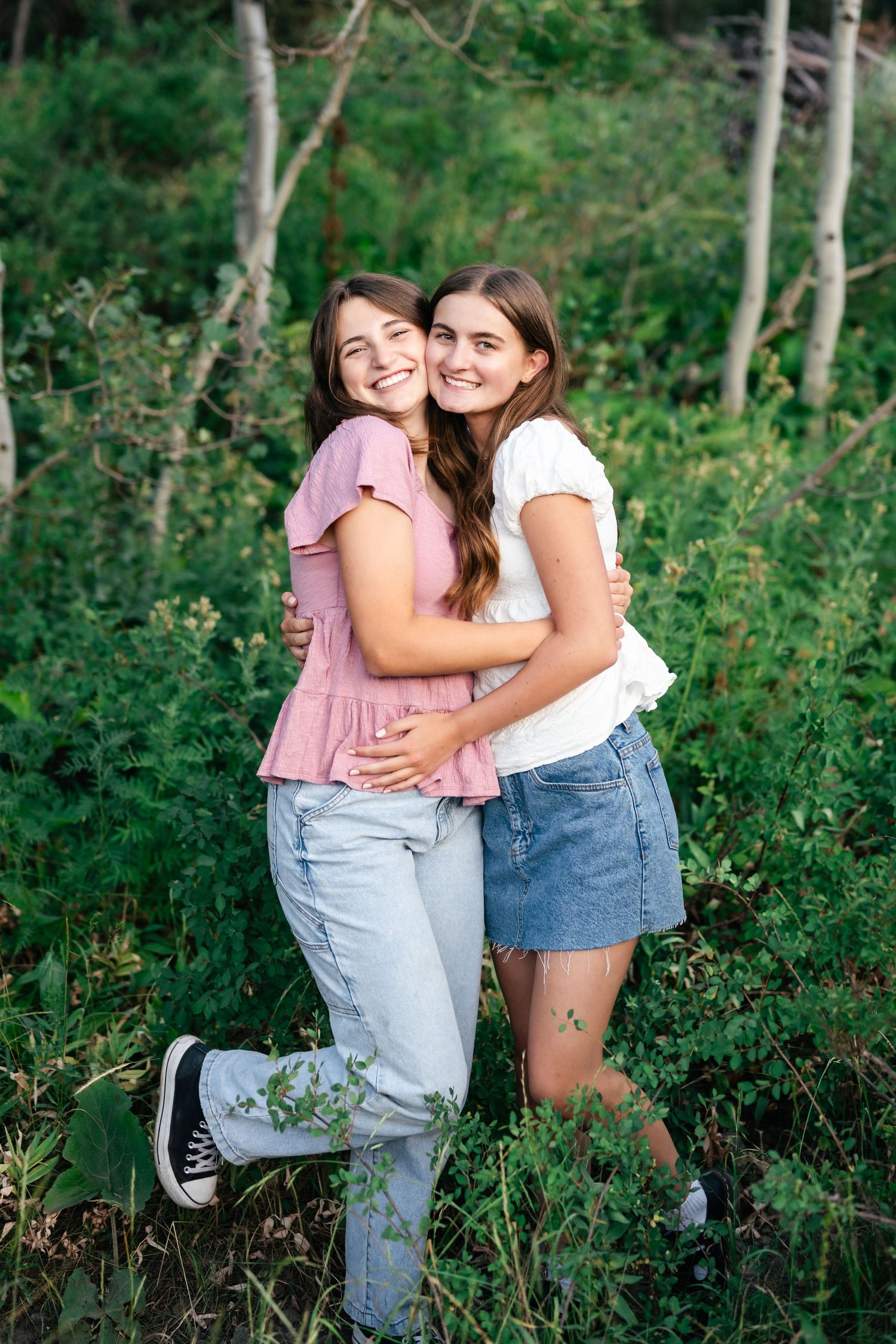 Two people share joyful embraces while standing among green foliage in a wooded area.