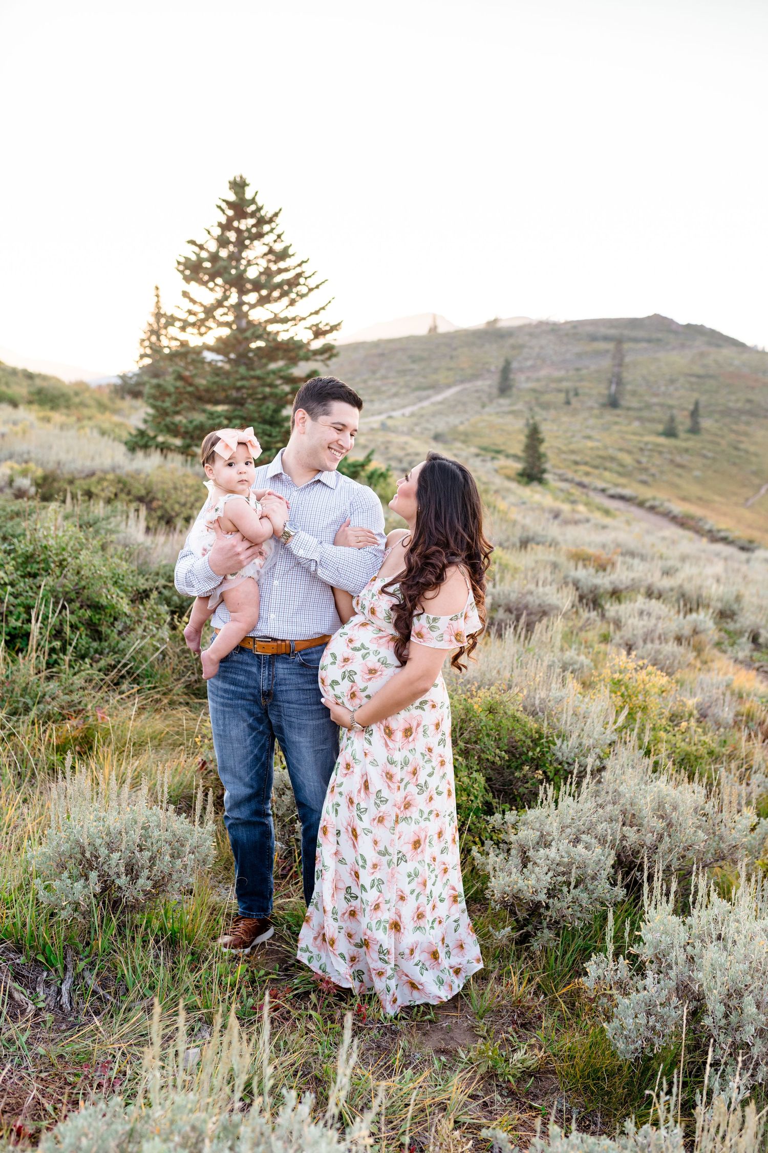 Family enjoys a tender moment together in a scenic mountain landscape with sagebrush and evergreen trees at sunset.