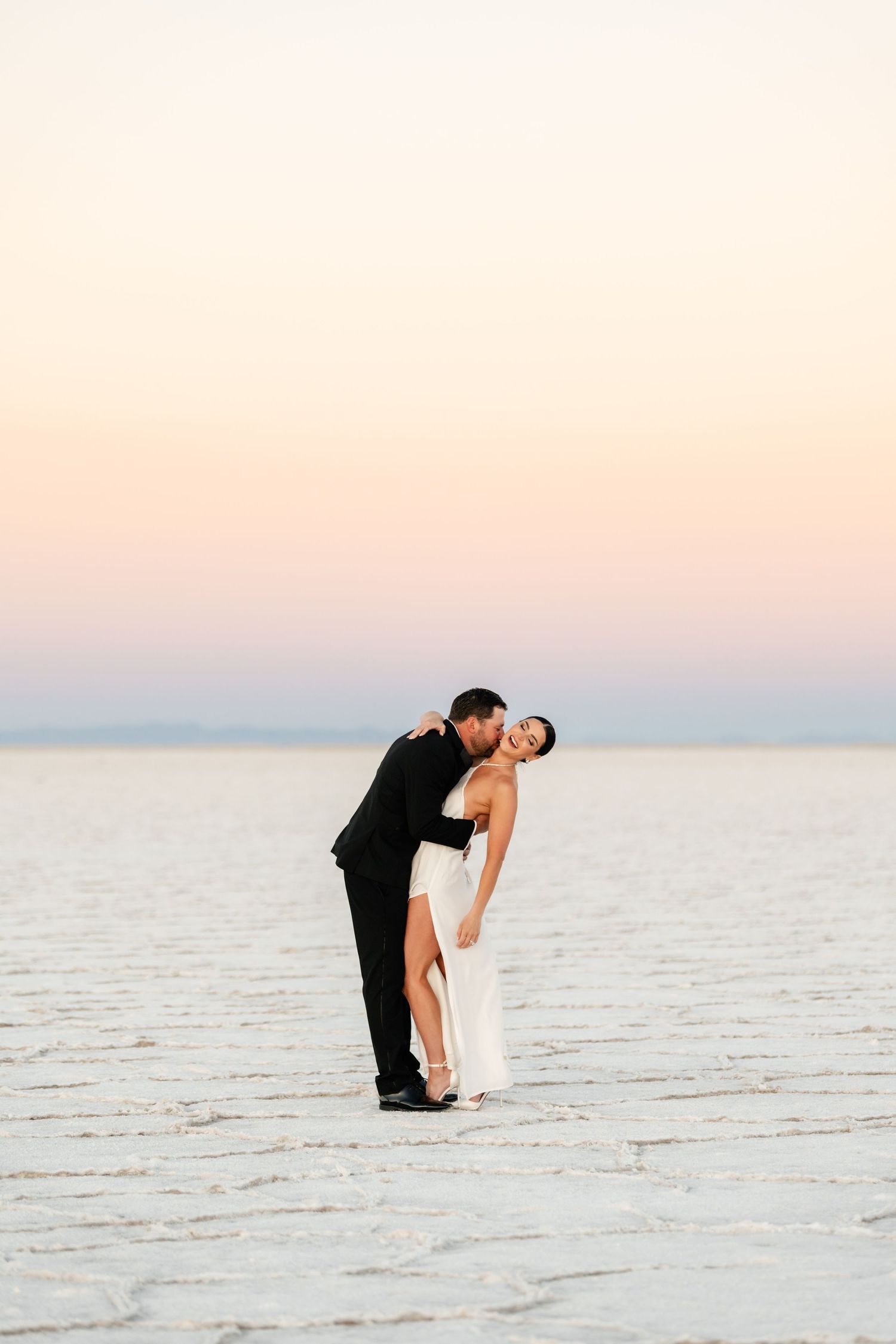Utah Salt Flats Photographer. Intimate moment between couple in formal wear on white salt flats at sunset.