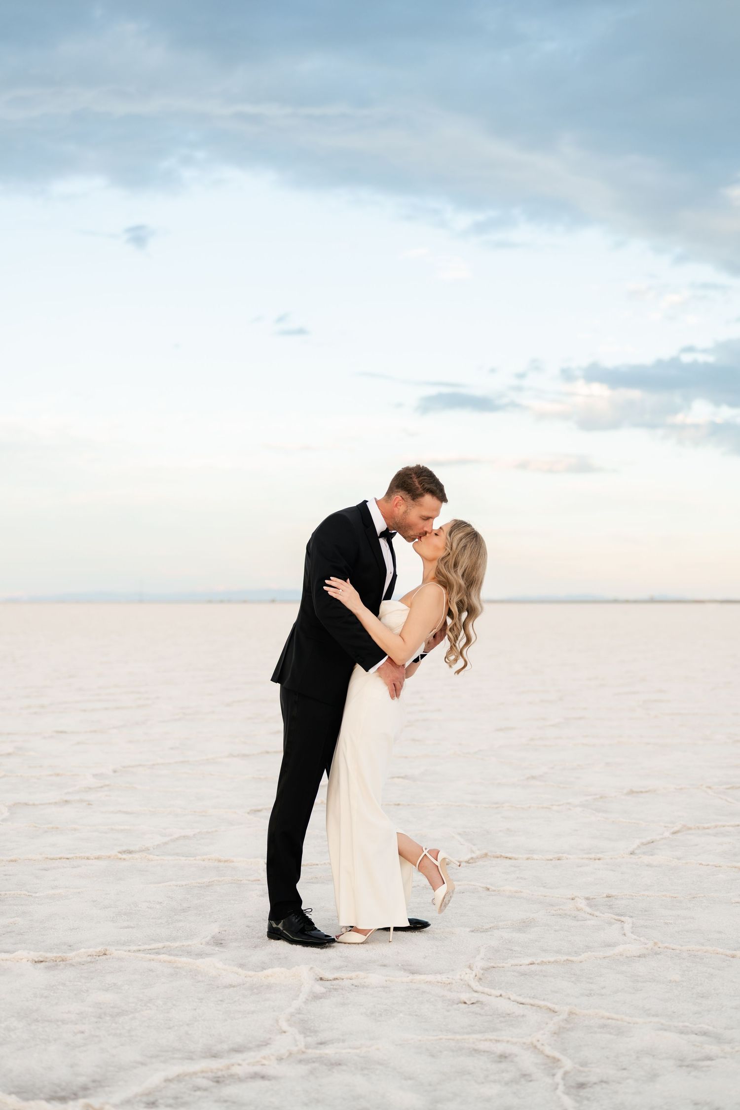 Salt Flats Elopement. A couple shares a romantic dip pose on white salt flats with a pastel sky backdrop during their wedding photoshoot.