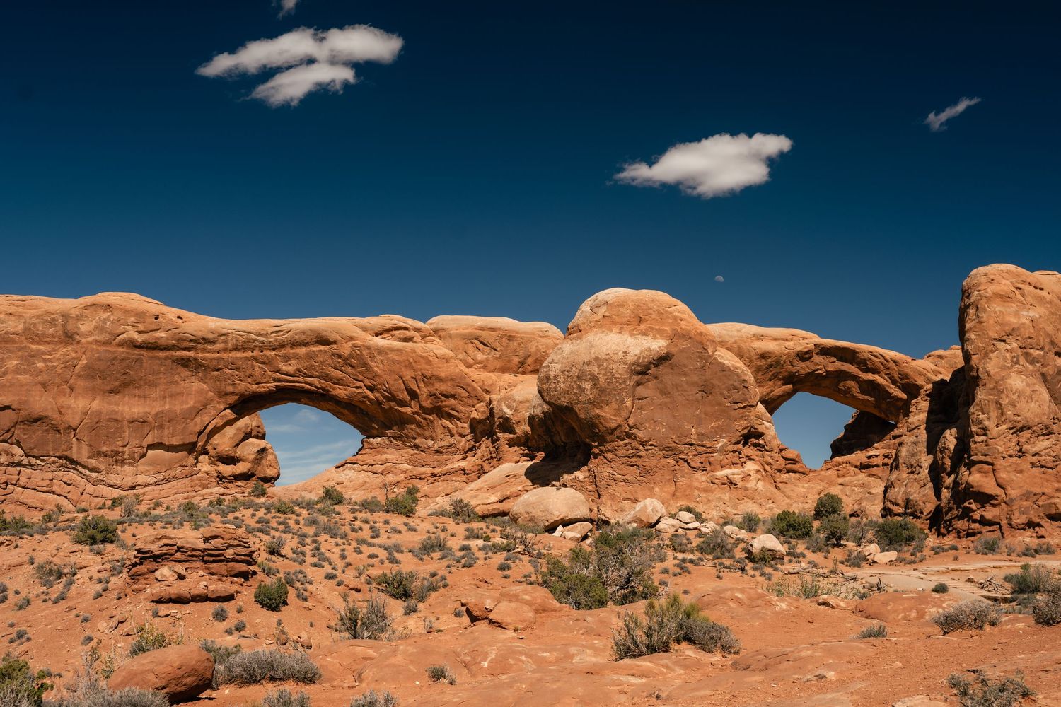 Natural stone arches span across red sandstone formations under a deep blue desert sky at Arches National Park.