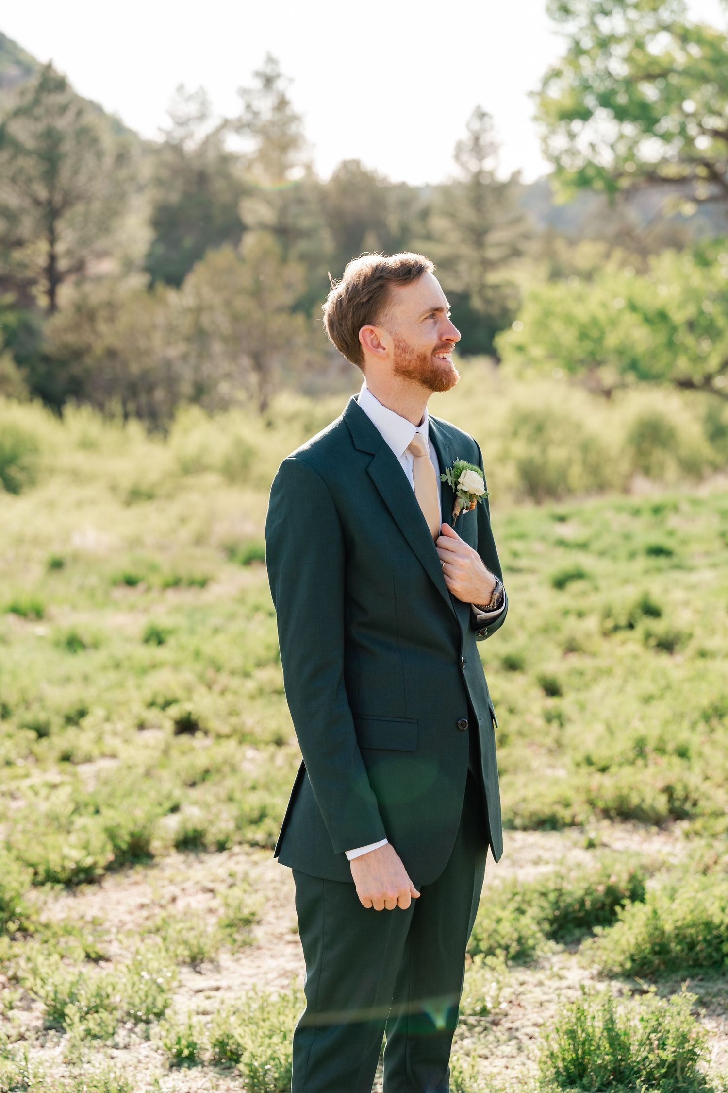 Groom in dark suit poses against natural landscape backdrop.