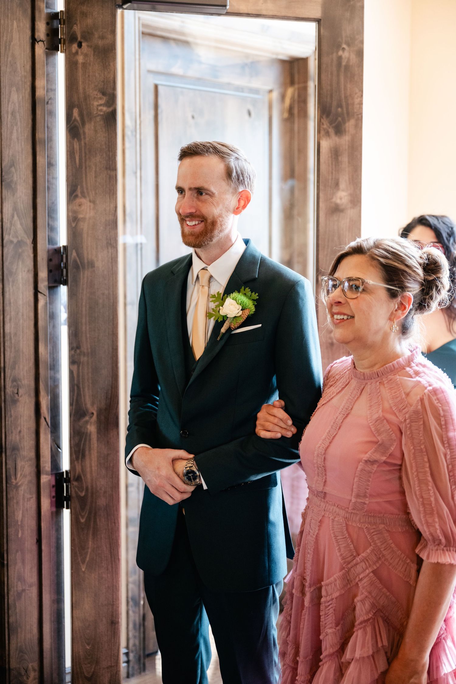 Wedding party members share joyful laughter in a rustic venue with wood-framed windows.