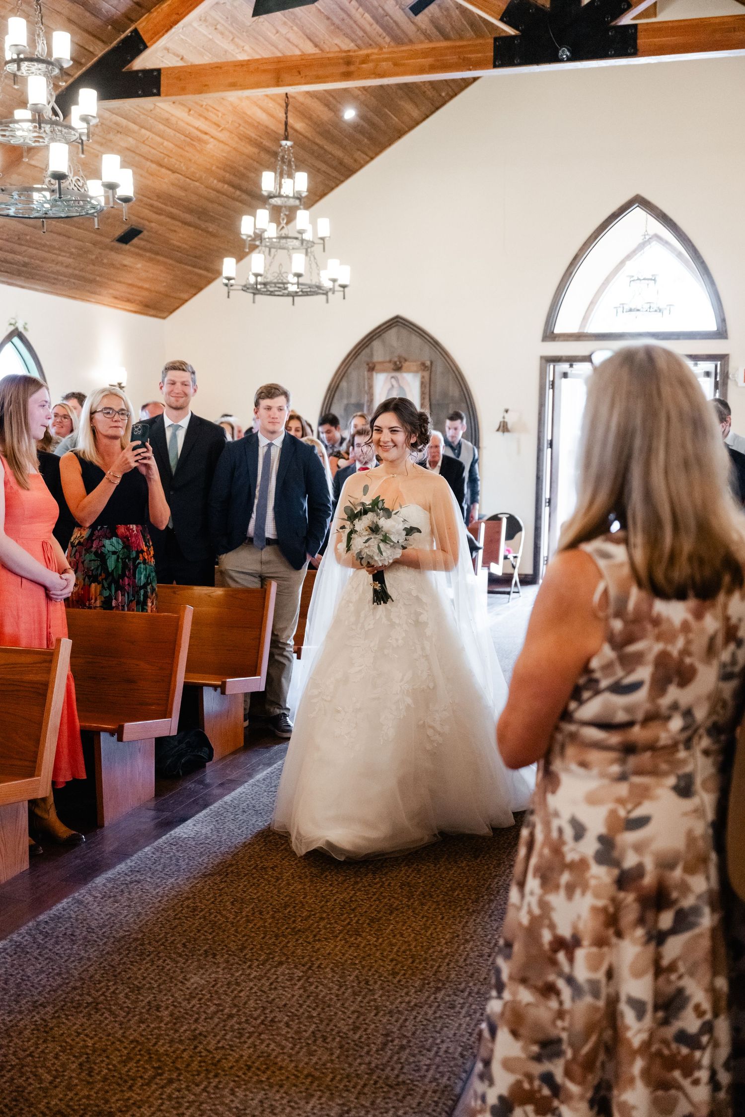 A sequence of wedding ceremony moments showing guests watching a couple walk down the aisle in a chapel with wooden ceilings.