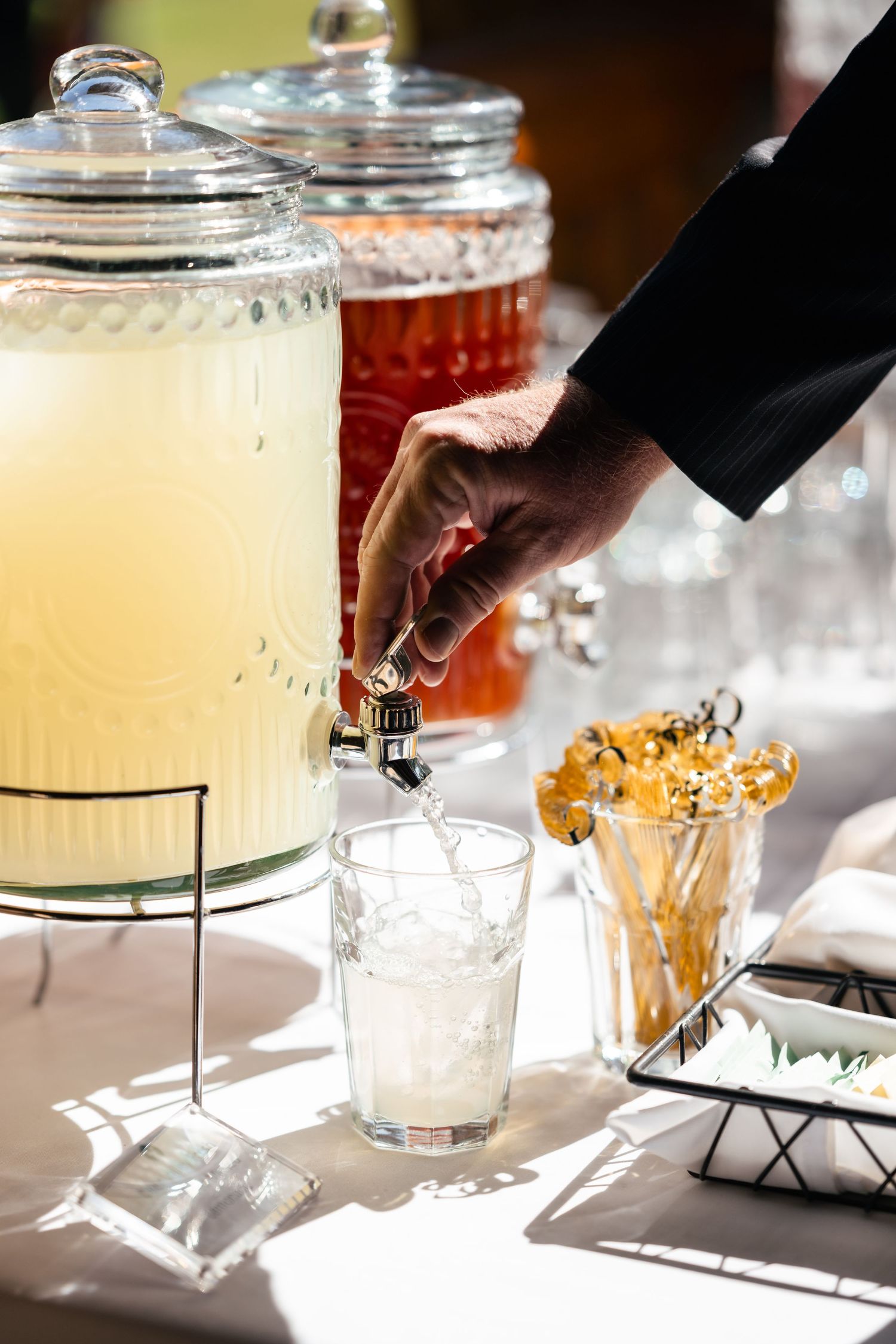Drink dispensers with clear liquid being poured into mason jars at a wedding beverage station.