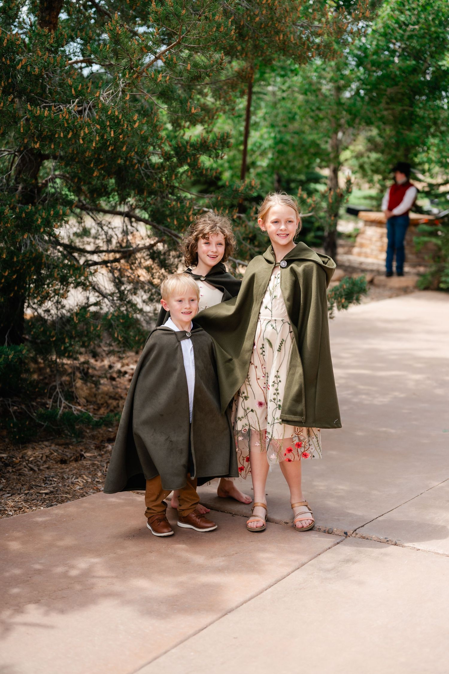 Two children in formal wear and capes playing together on outdoor pathway.