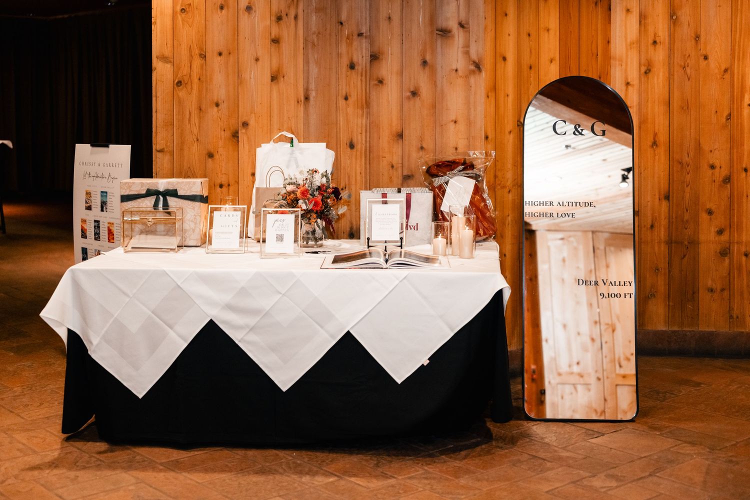 Reception tables set with white linens inside a rustic wooden venue with warm lighting.