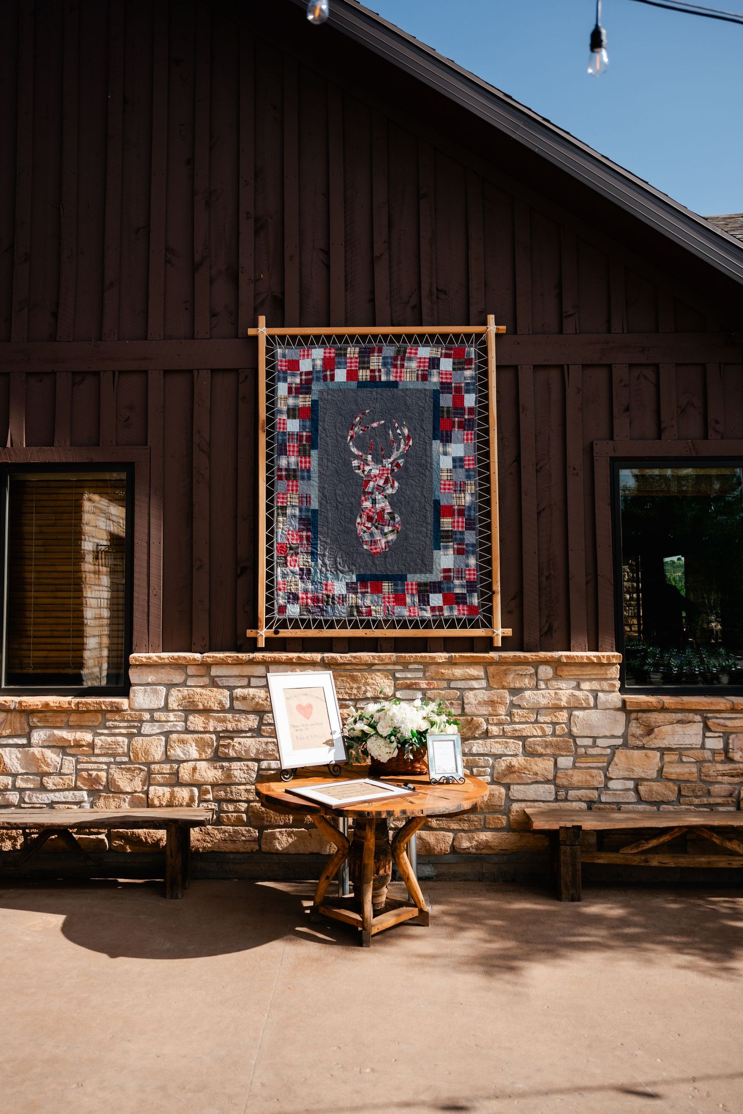 Rustic brown barn exterior with stone base and decorative quilts displayed on wooden hangers.