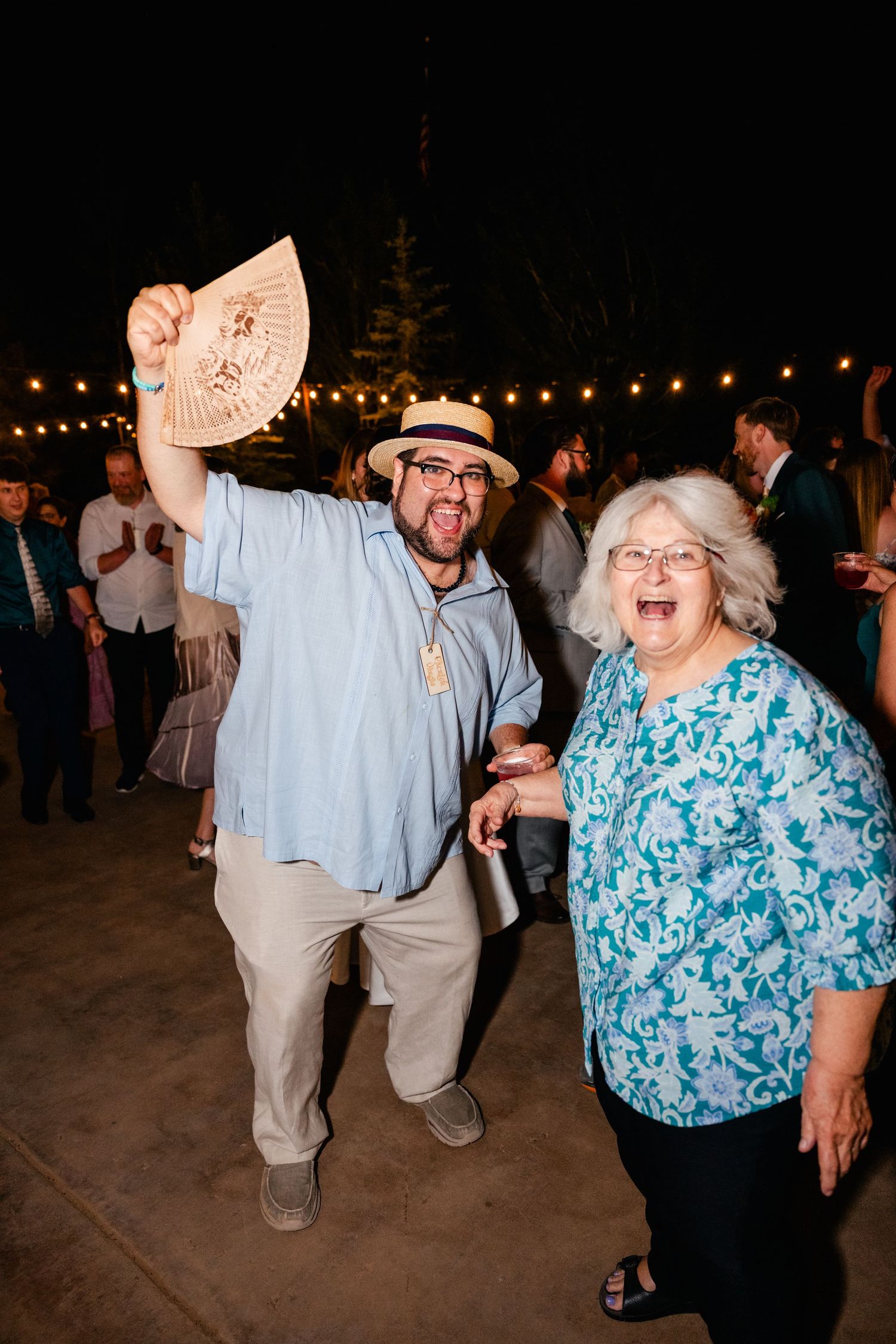 Lively wedding reception dance party with string lights creating a festive outdoor atmosphere.