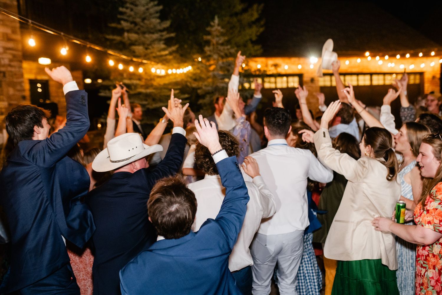 Wedding guests raise their hands in celebration during an outdoor evening reception.