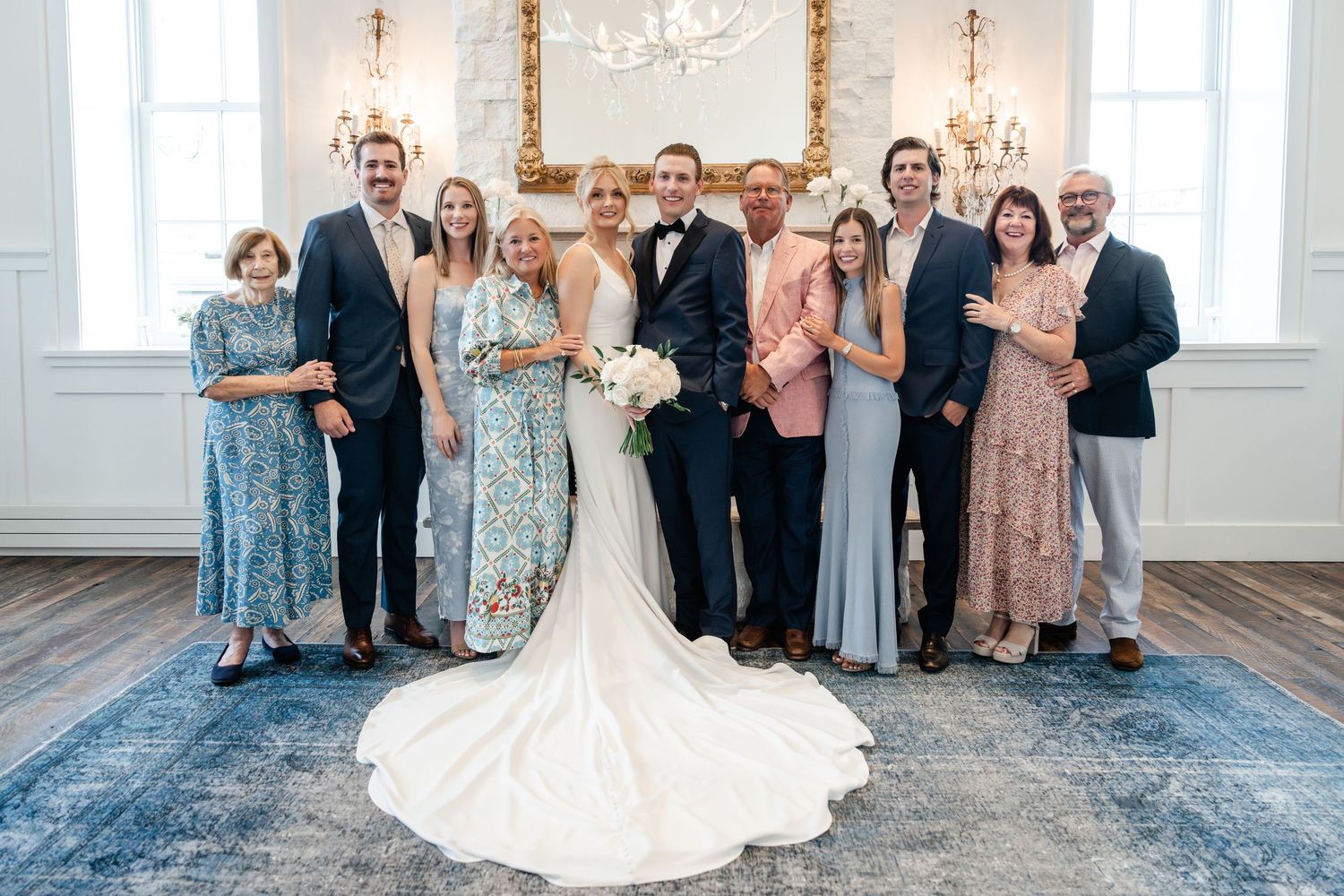 Wedding party poses in elegant white chapel interior with chandelier and natural lighting.