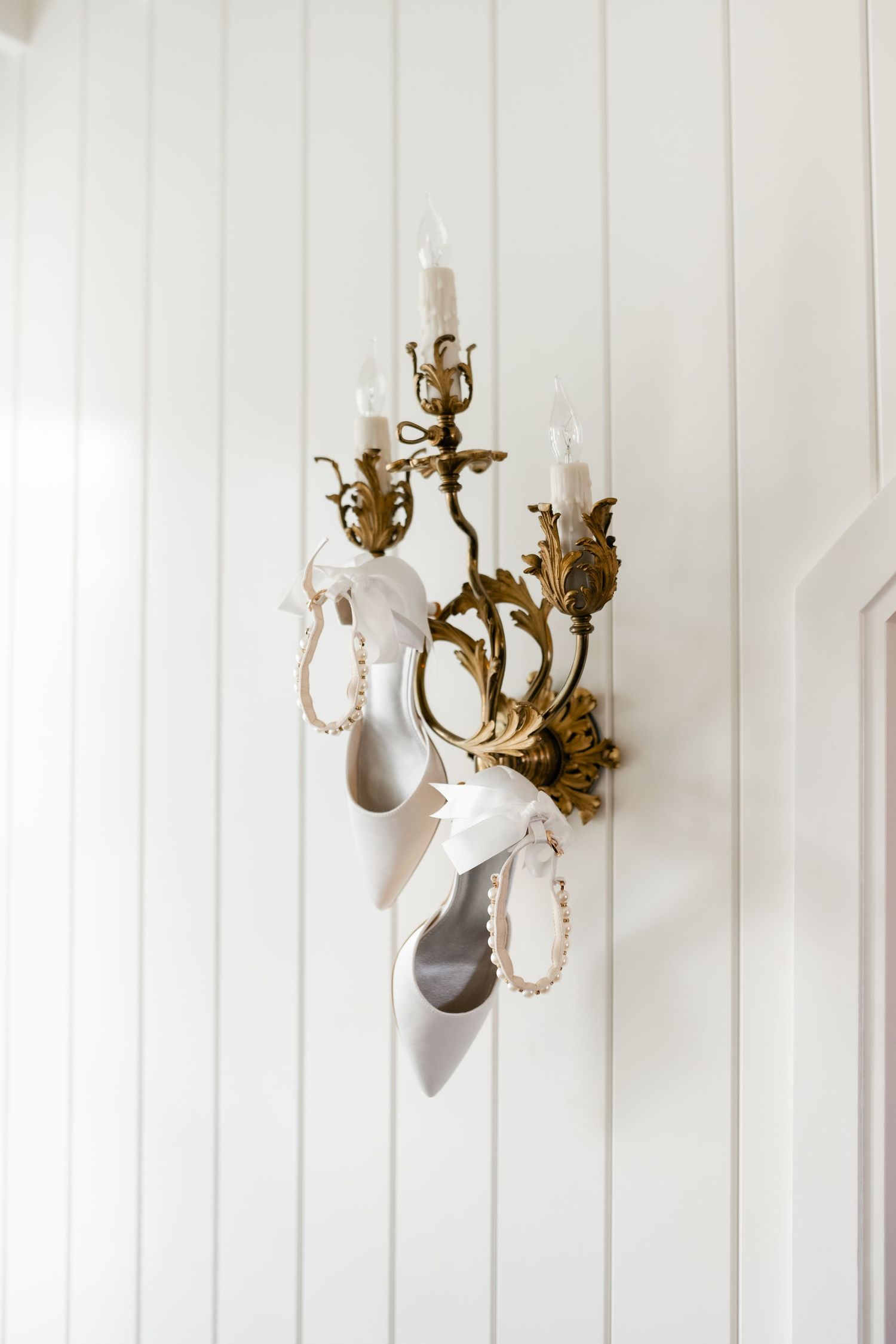 White decorative wall sconces and brass chandelier fixtures mounted on white paneled wall.
