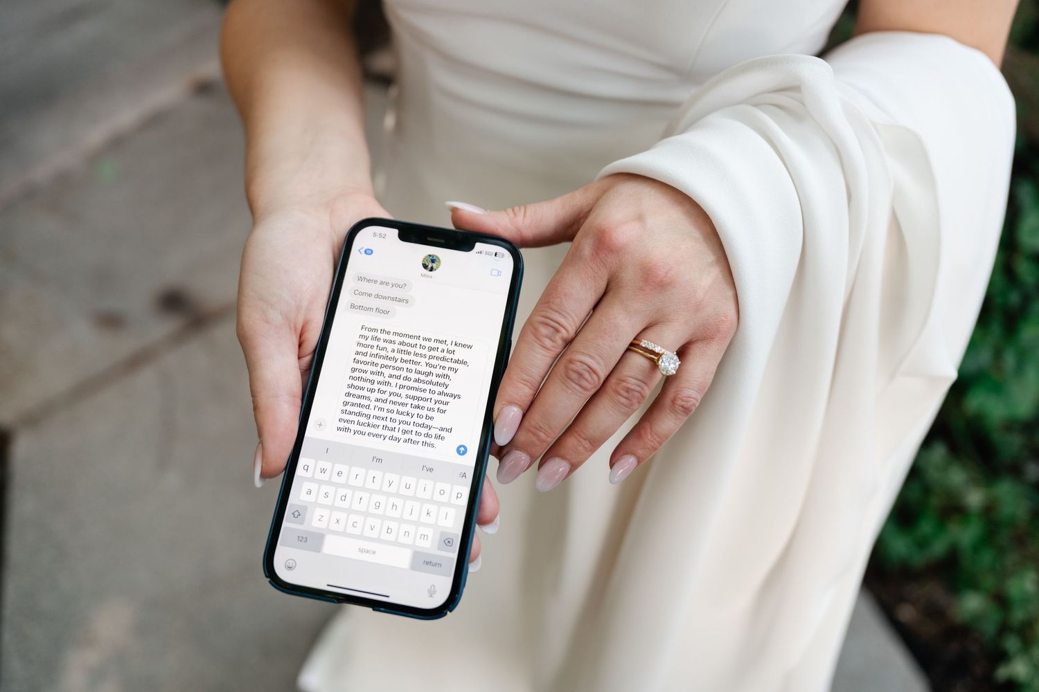 Person in white dress holds a smartphone displaying text while sitting outdoors.