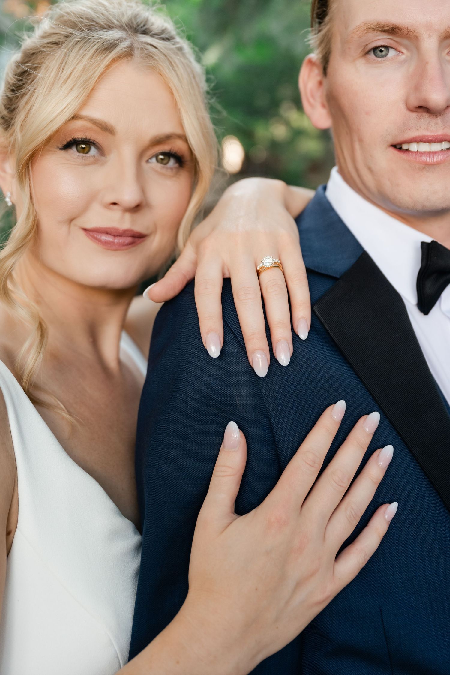 Close-up details of wedding rings and hands against a navy suit backdrop.