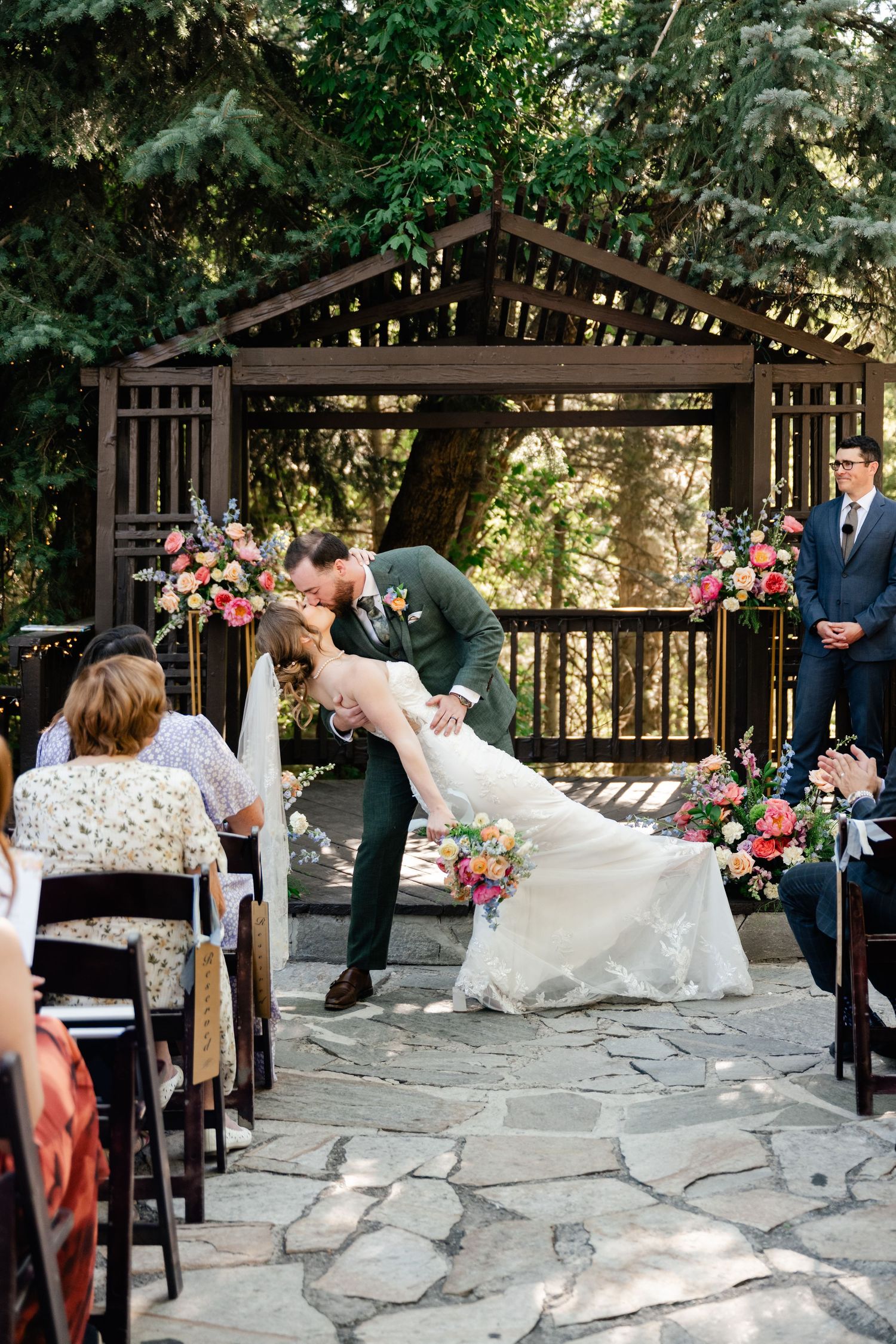 Outdoor wedding ceremony taking place under a rustic wooden gazebo with stone flooring.