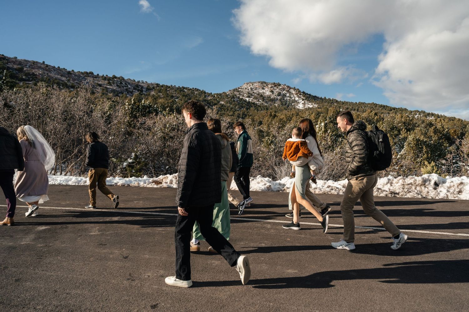 People walking along a snow-dusted path with dramatic red rock cliffs in the background.
